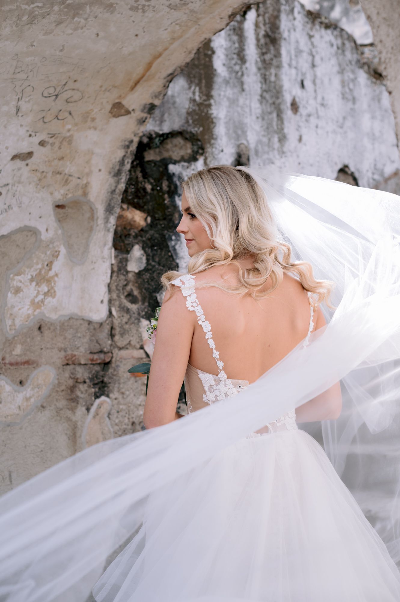 Ethereal bridal portrait capturing flowing veil and open-back wedding dress details.