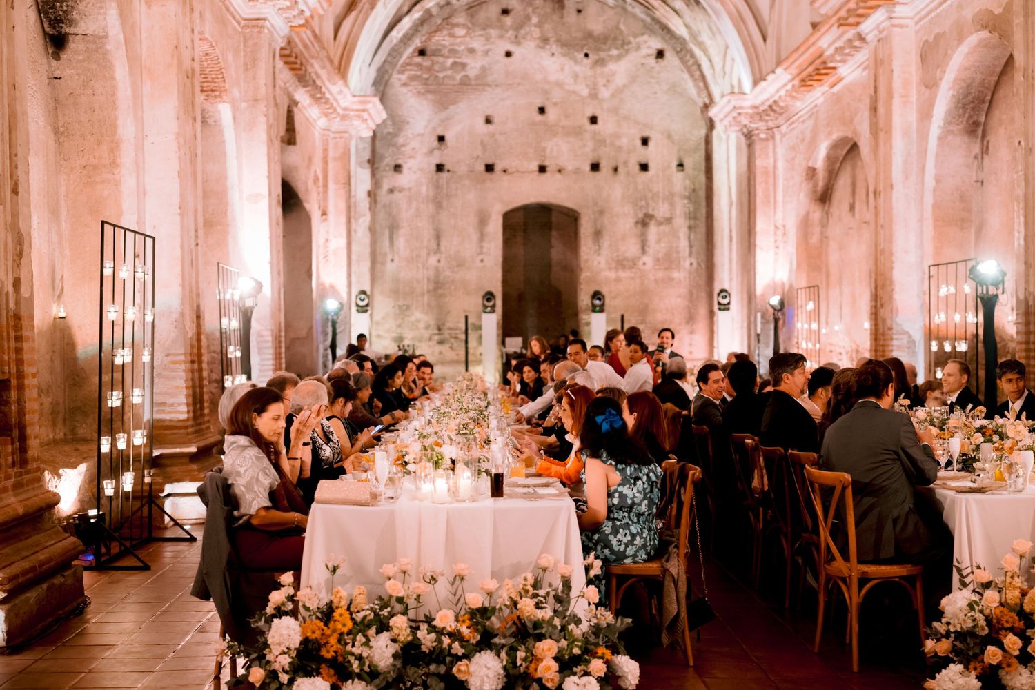 Wedding reception in progress inside historic chapel with vaulted ceilings and floral decorations.