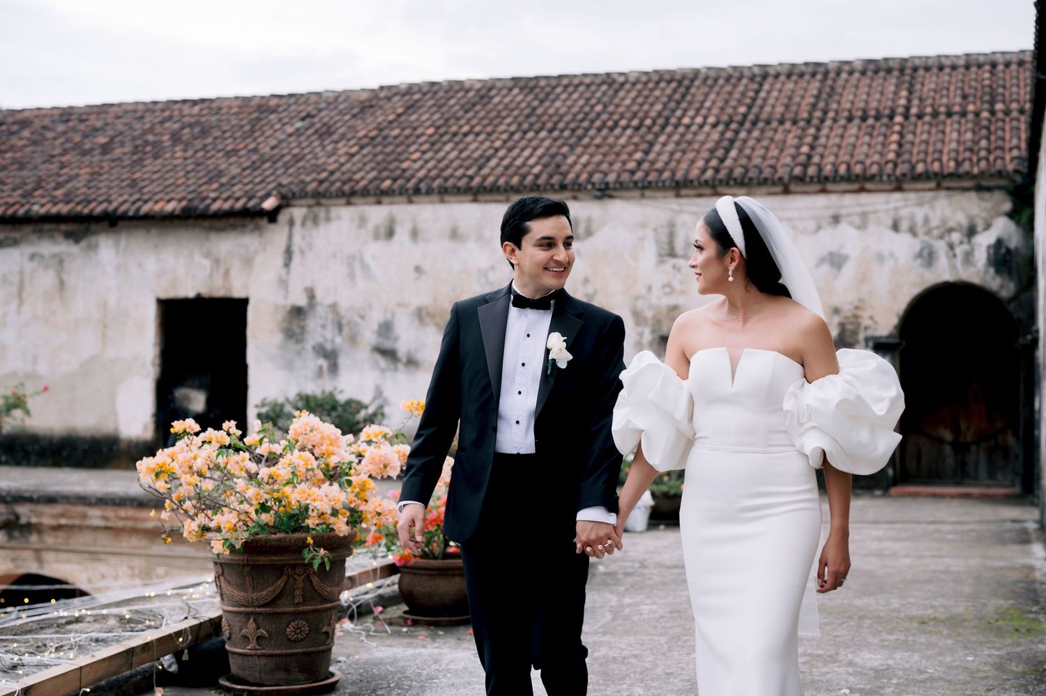 A classic wedding scene with a couple walking past terra cotta planters at a rustic venue.