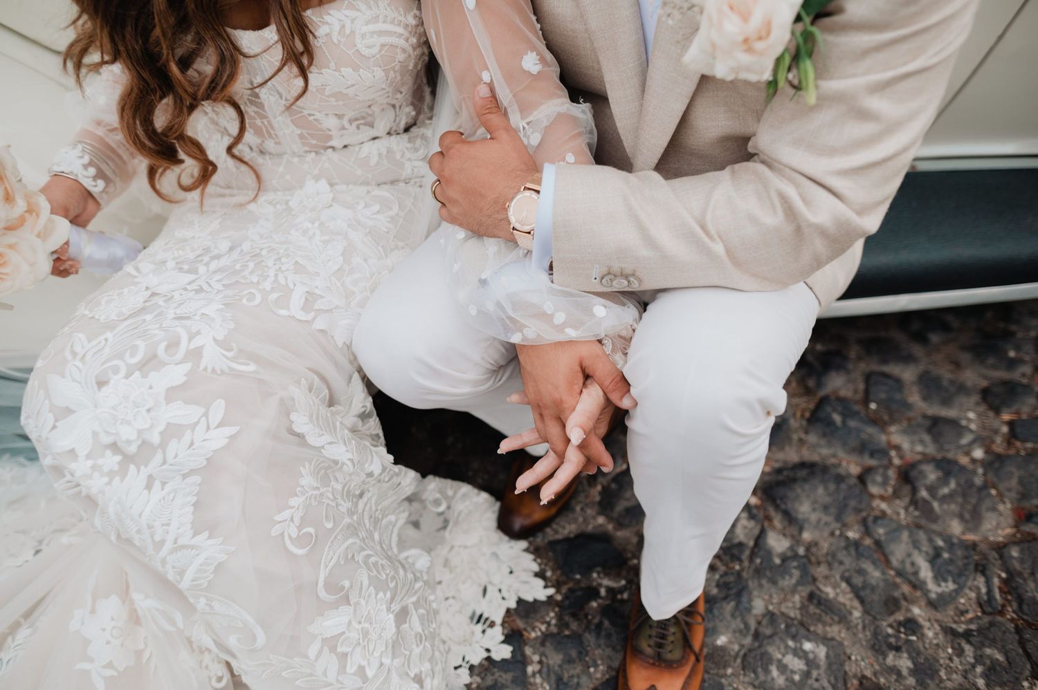 Close up of wedding couple's hands and lace dress details against stone ground.