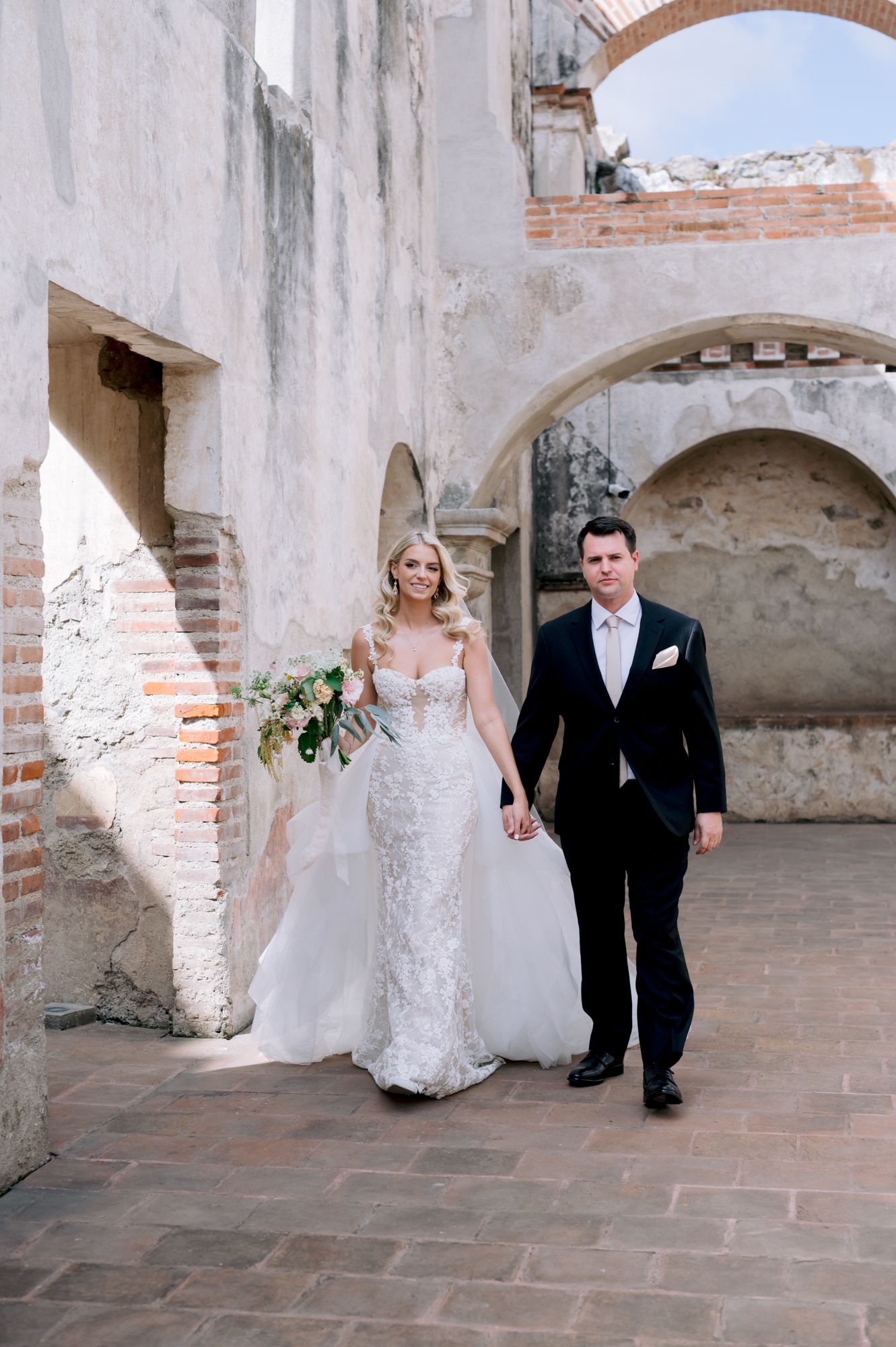 A newlywed couple walking through historic stone archways at their destination wedding.