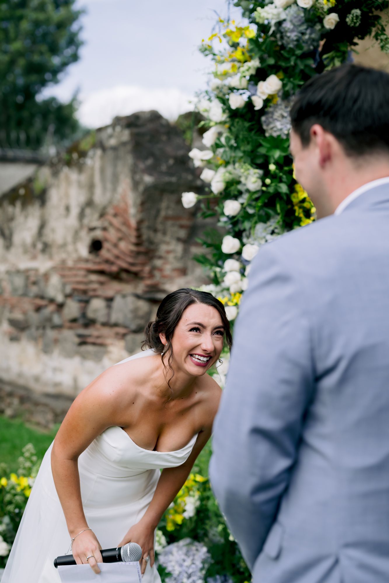Joyful wedding moment captured beside floral arch and ancient stone walls.