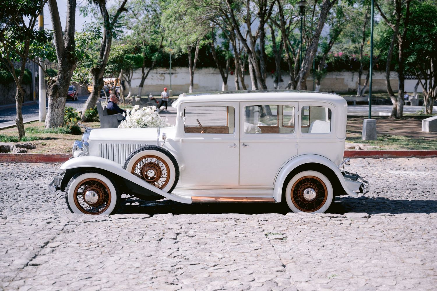 Vintage white antique car parked on gravel road under trees.