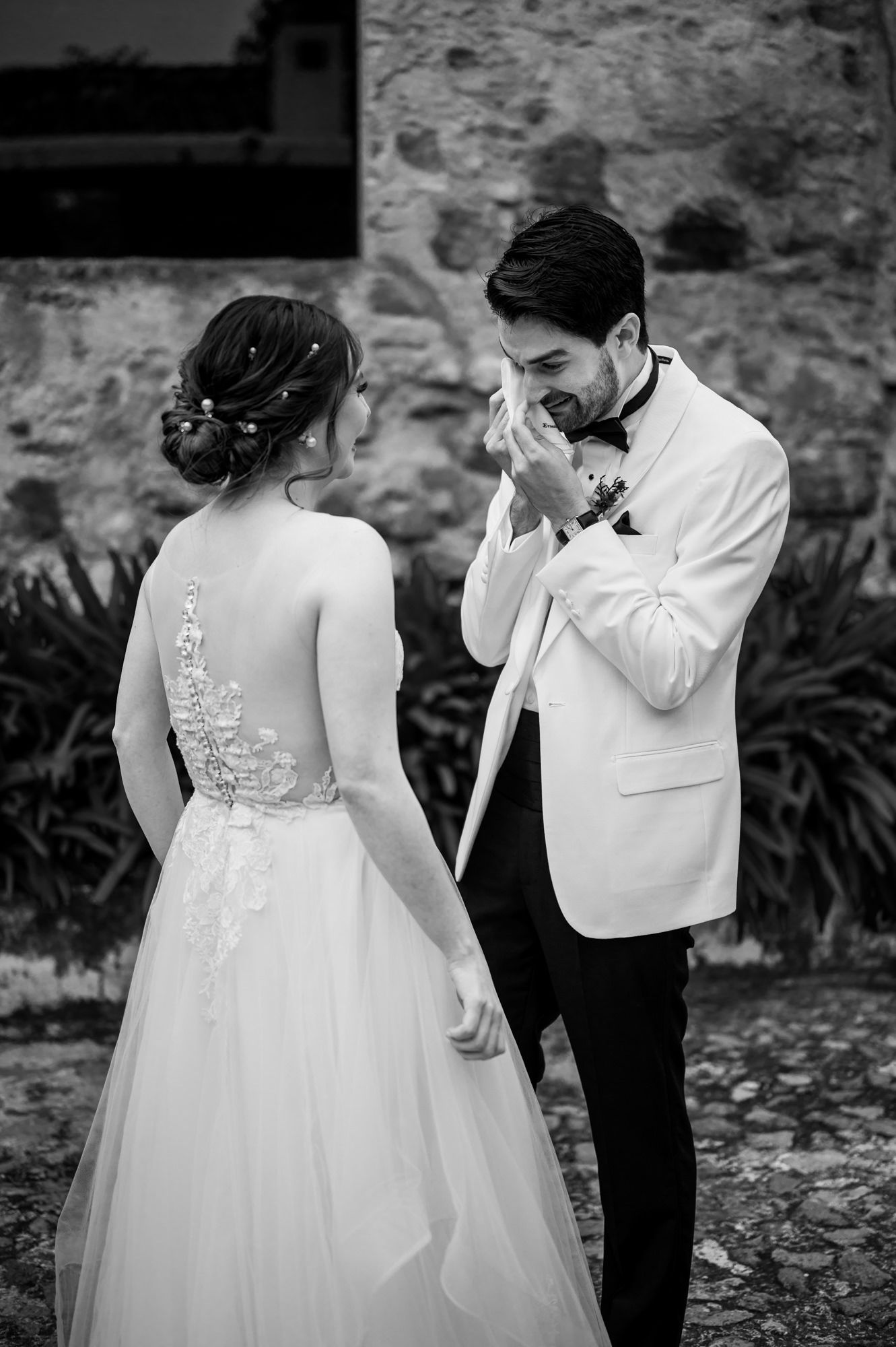 Black and white capture of emotional wedding first look by stone wall.