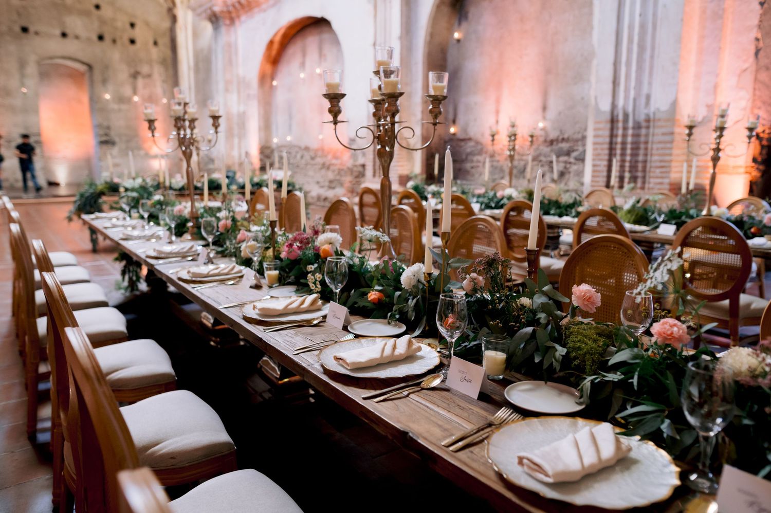 Long wooden reception table adorned with candelabras and floral arrangements in stone cathedral setting.