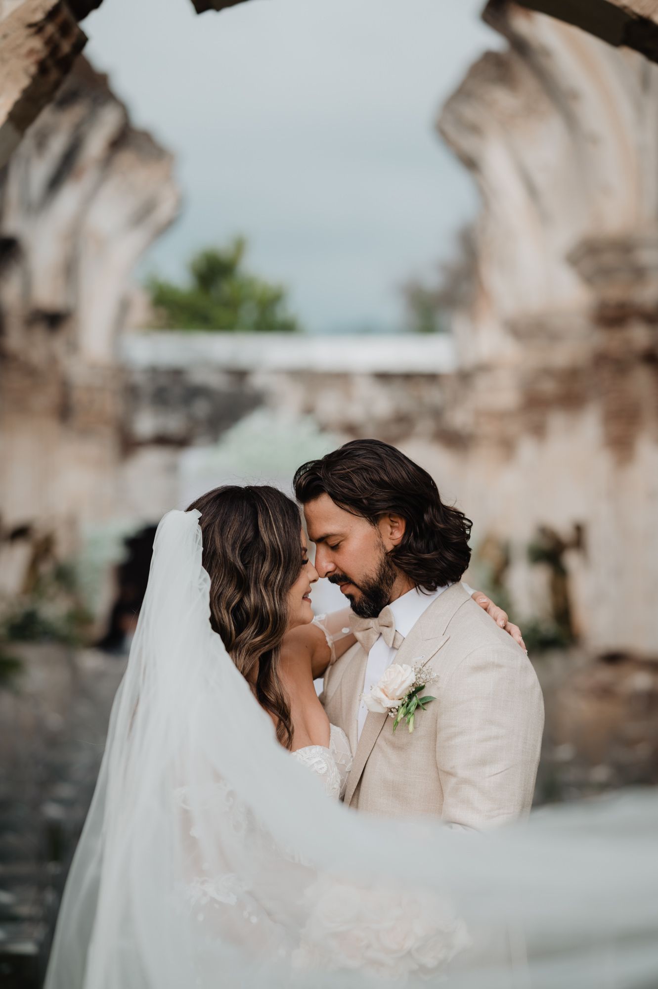 Romantic wedding moment captured against weathered stone architecture and green landscape.