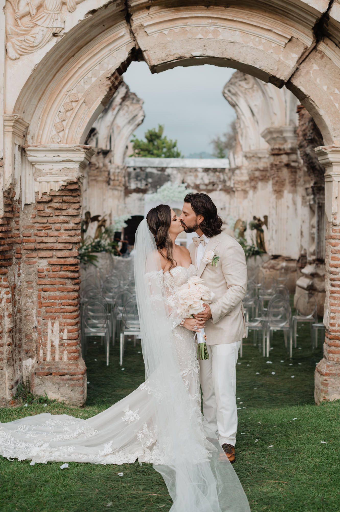 A couple shares a romantic moment under ancient stone arches in a garden wedding setting.