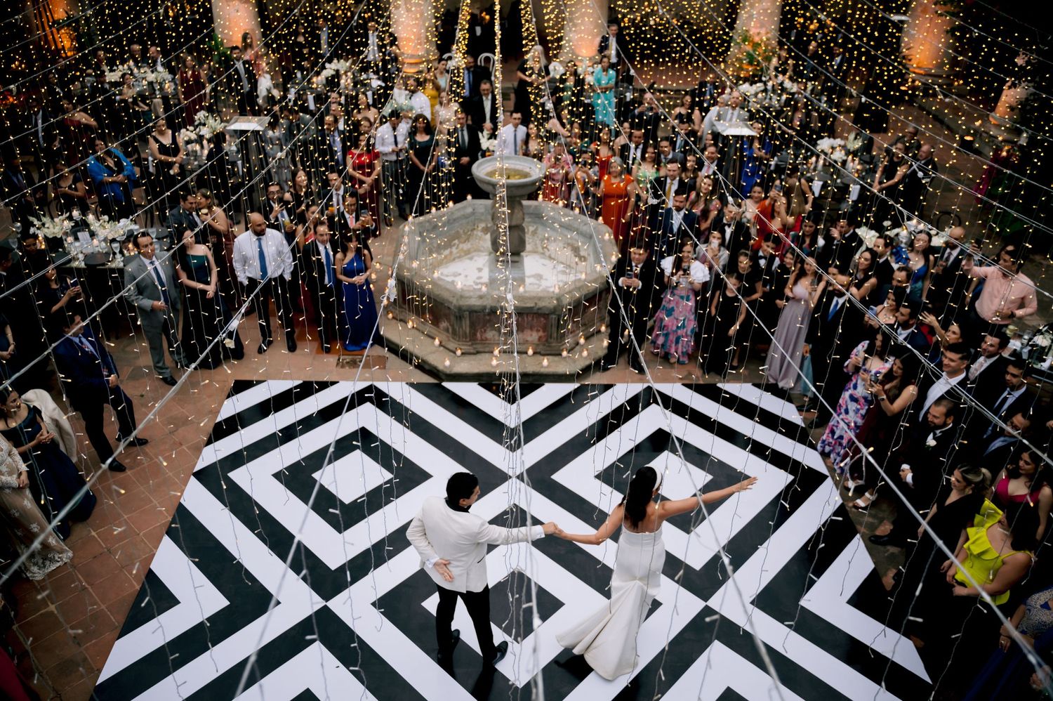 Aerial view of couple dancing on geometric black and white dance floor surrounded by guests.