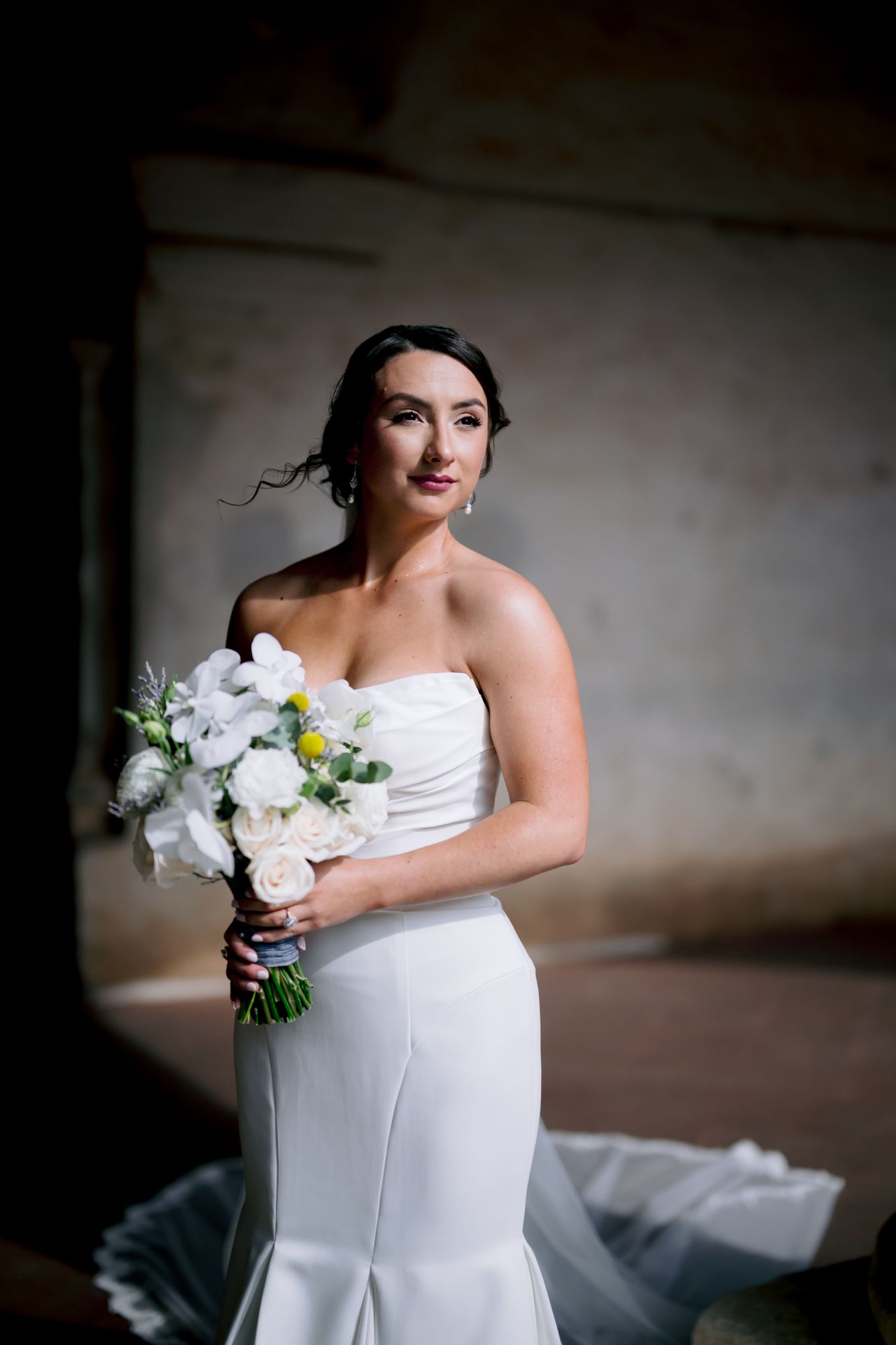 Dramatic bridal portrait with white floral bouquet against textured wall background.