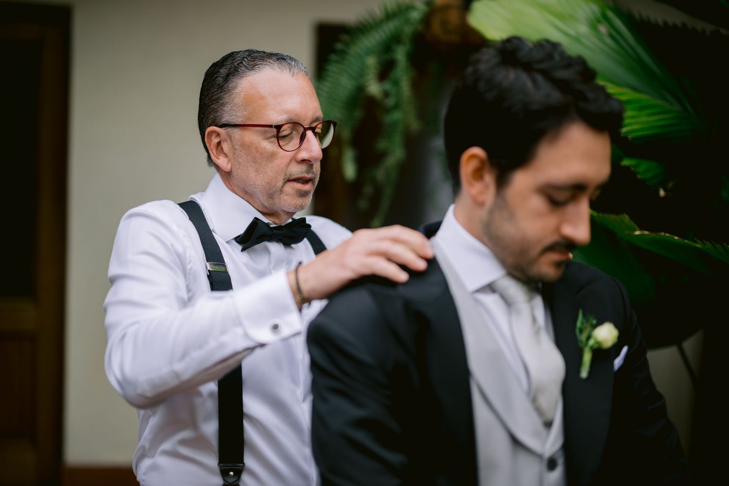 A formal dressing scene with white shirt and suspenders against a tropical backdrop.
