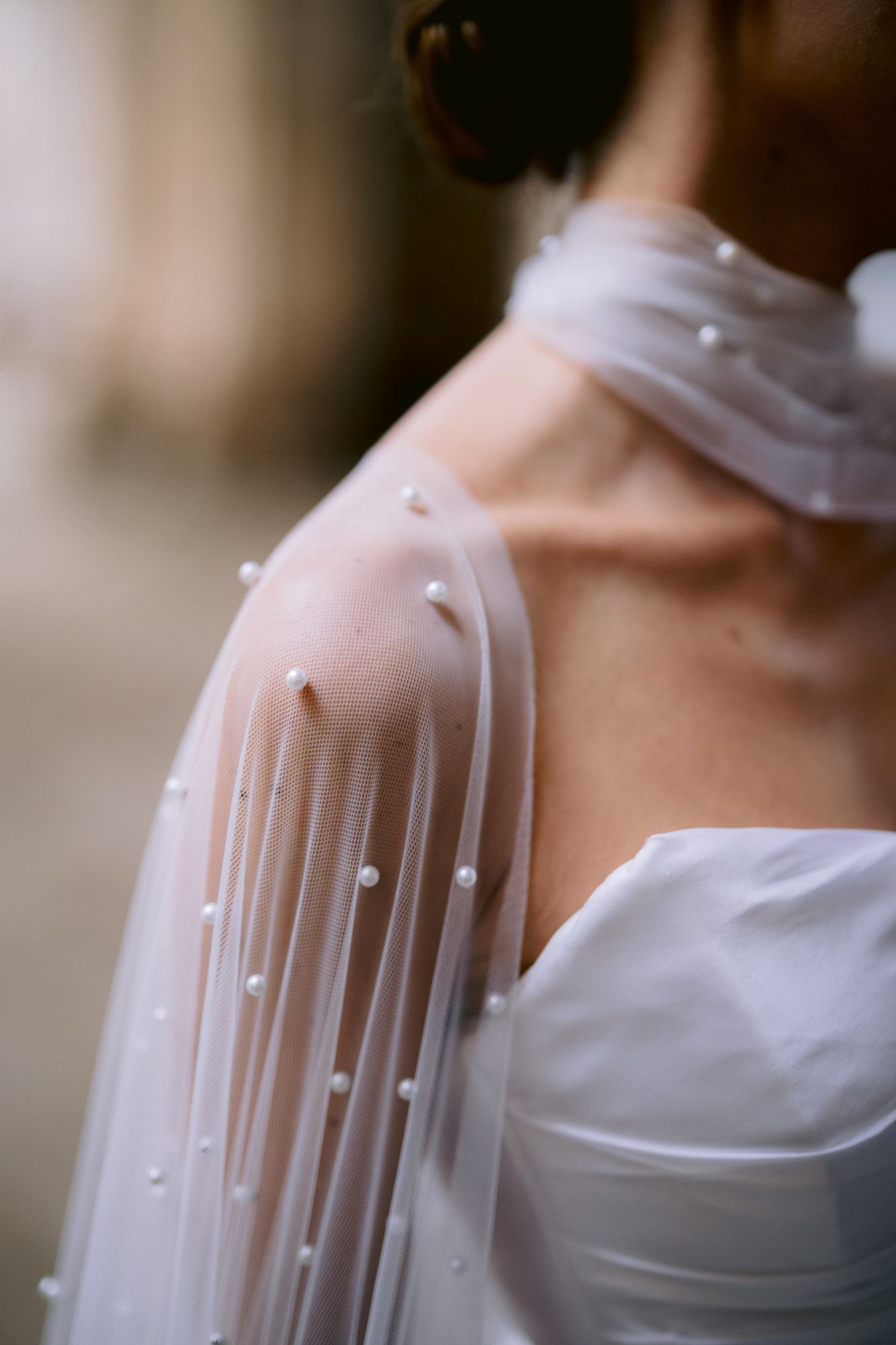 Close-up detail of delicate pearl-studded sheer wedding cape sleeve against white dress.