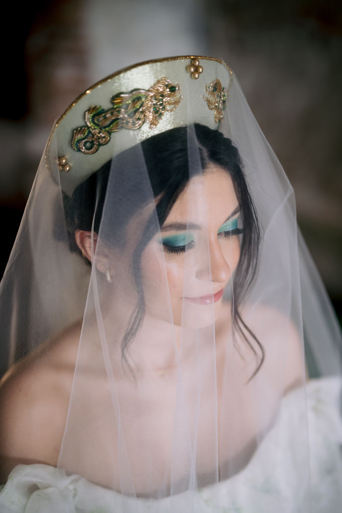 Ethereal bridal portrait highlighting an ornate gold crown and sheer veil with turquoise eye makeup.