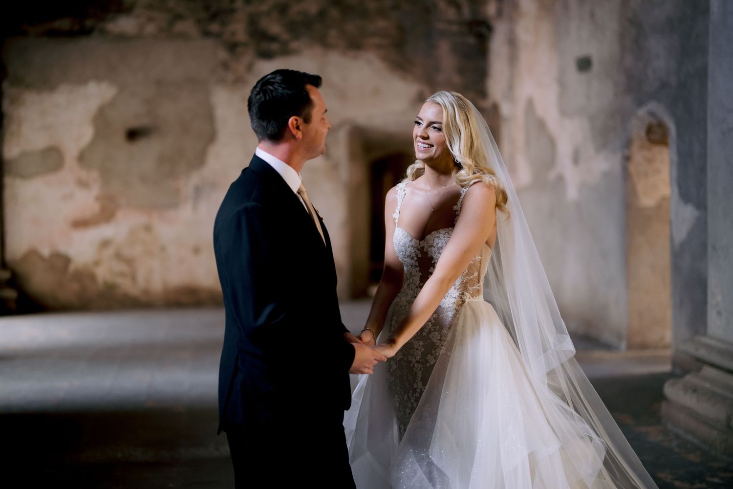 A couple shares a romantic moment under historic stone arches on their wedding day.