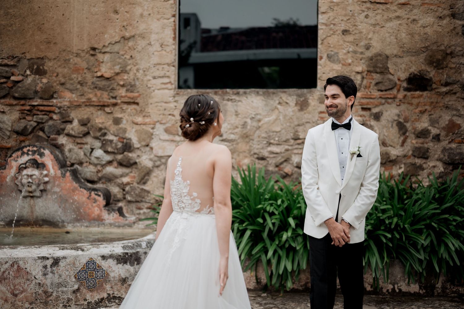 A romantic first look wedding moment against a rustic stone wall with lush greenery.