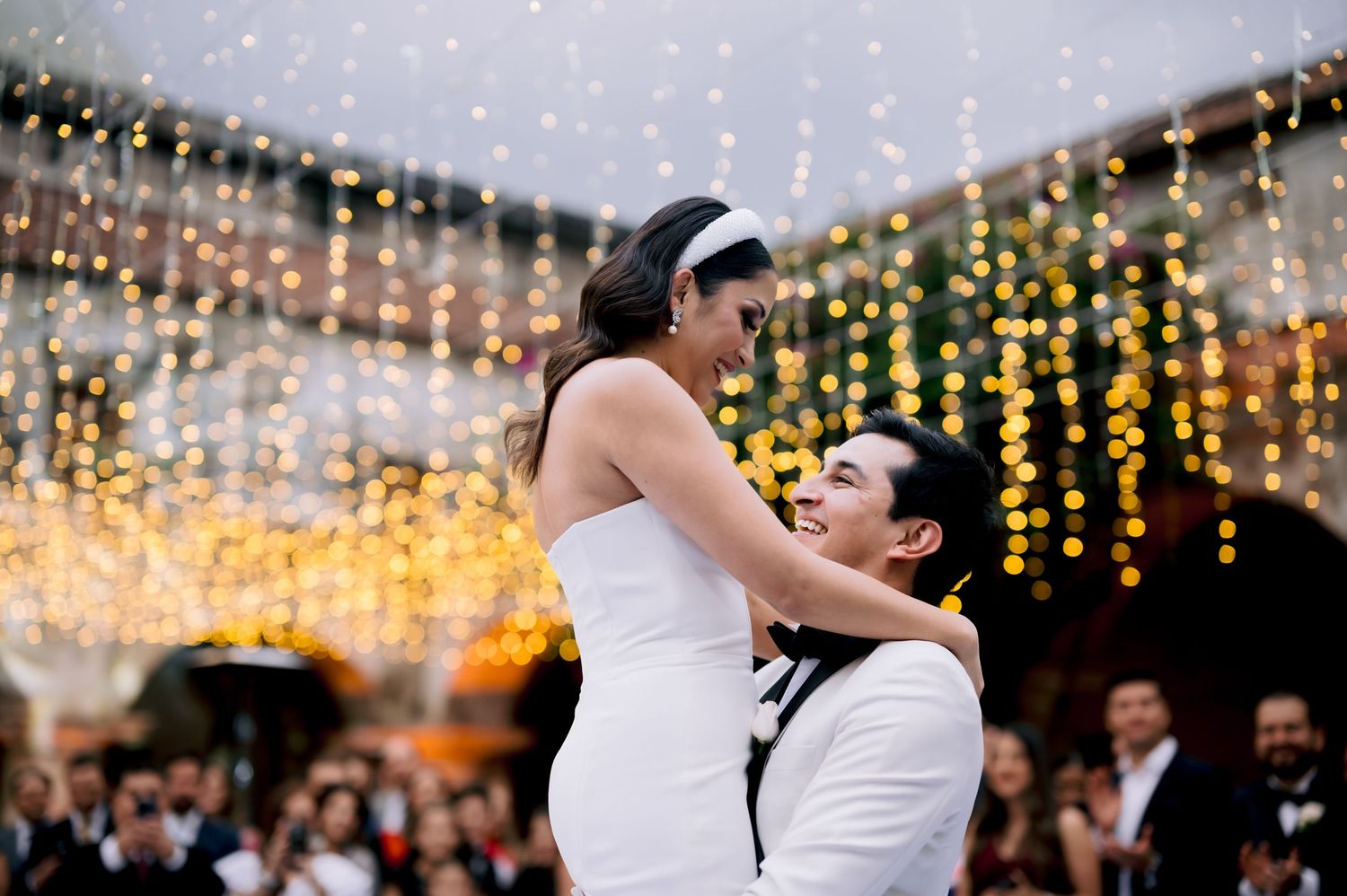 Wedding couple dancing under romantic string lights at outdoor evening reception.