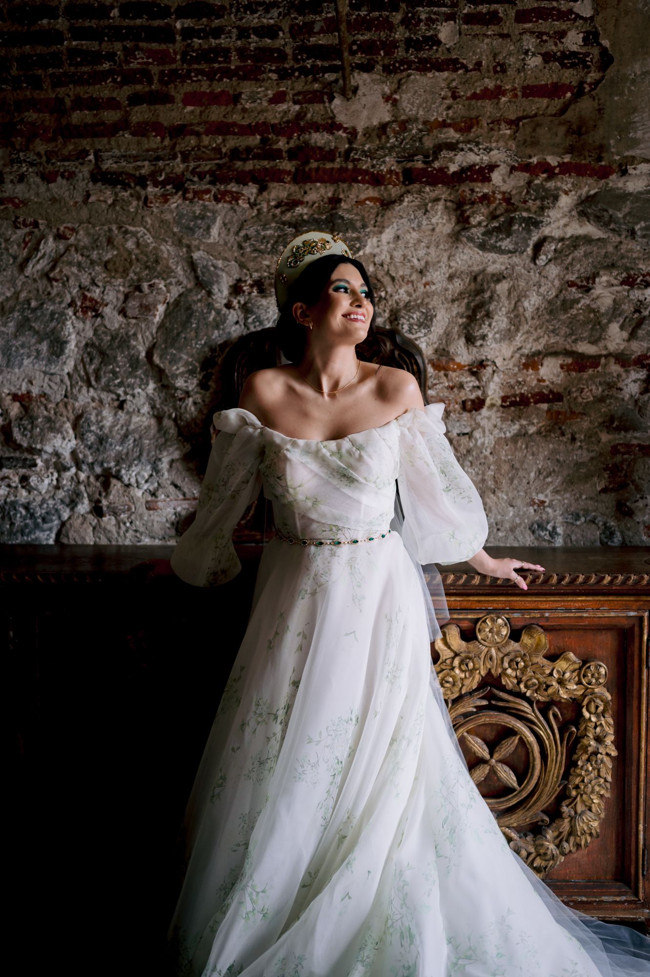 Classic bridal portrait features an off-shoulder wedding gown against weathered brick wall background.