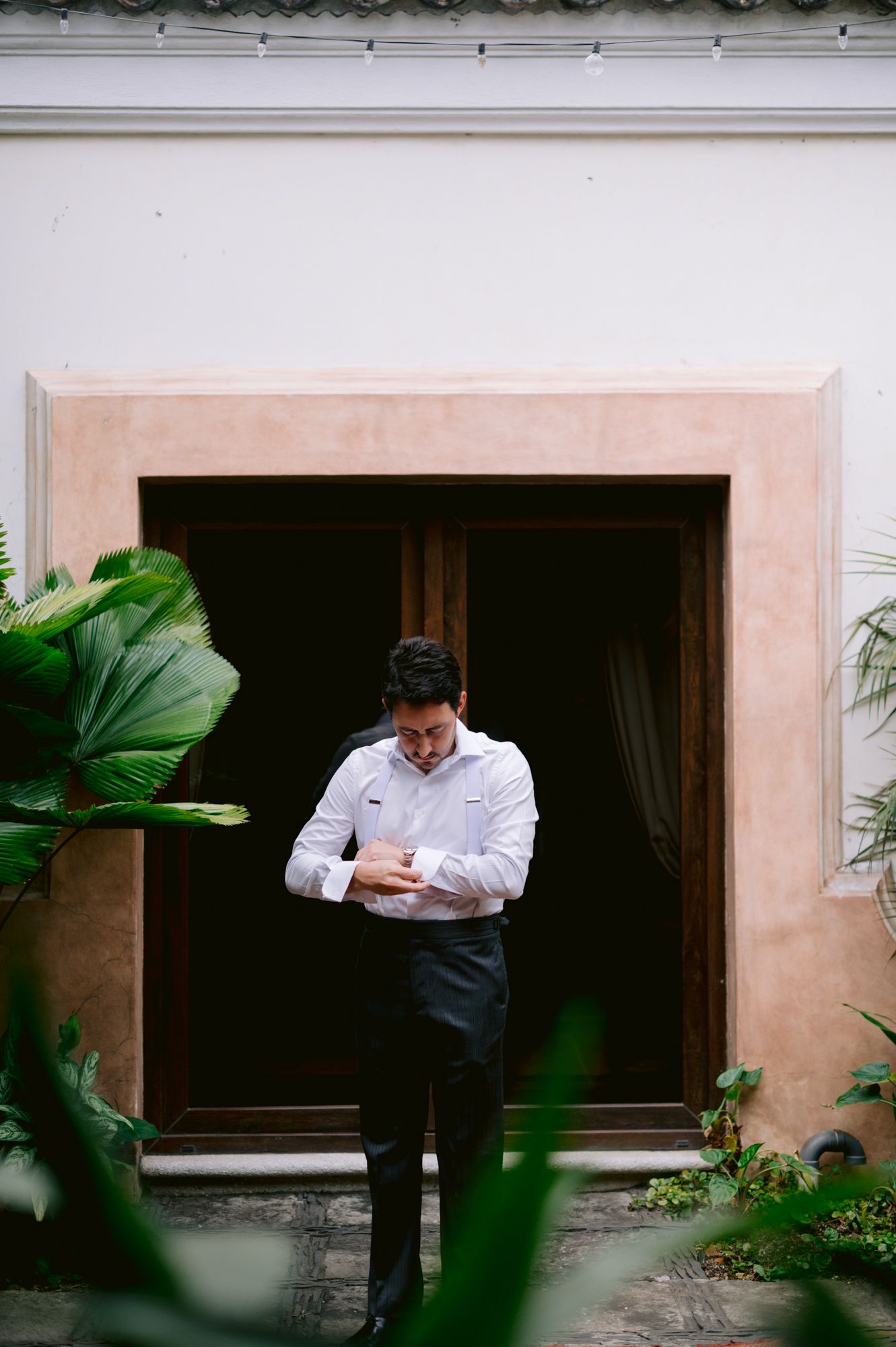 A formal occasion preparation scene with tropical plants framing a doorway.