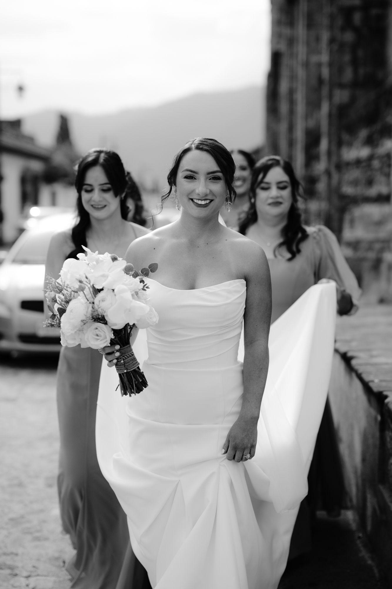 Classic black and white wedding photo of bride and bridesmaids walking along stone pathway.