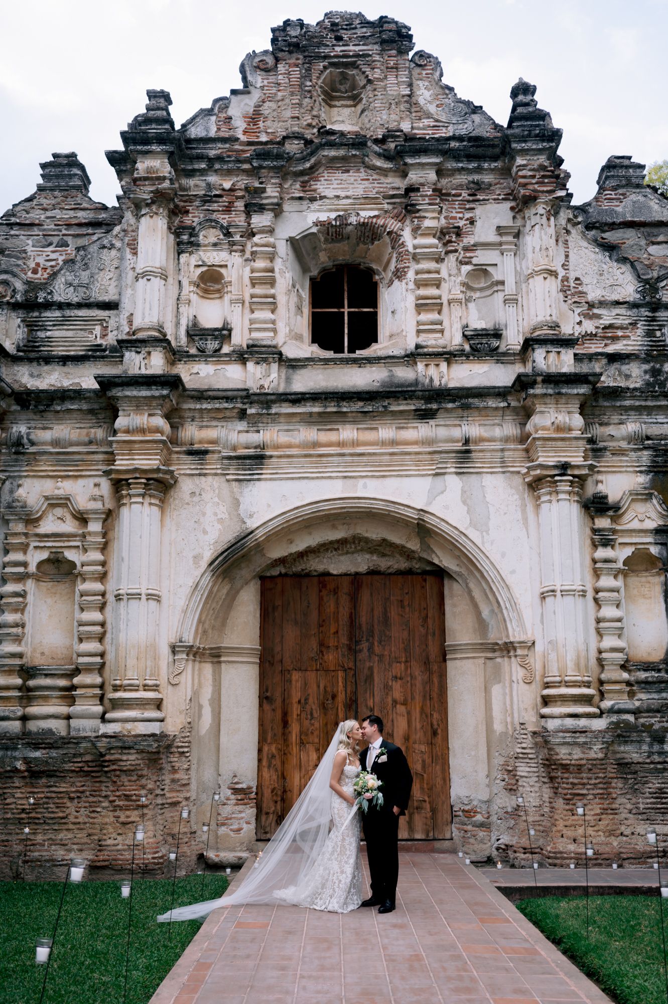 Newlyweds share an intimate moment in front of massive wooden doors of a historic church.
