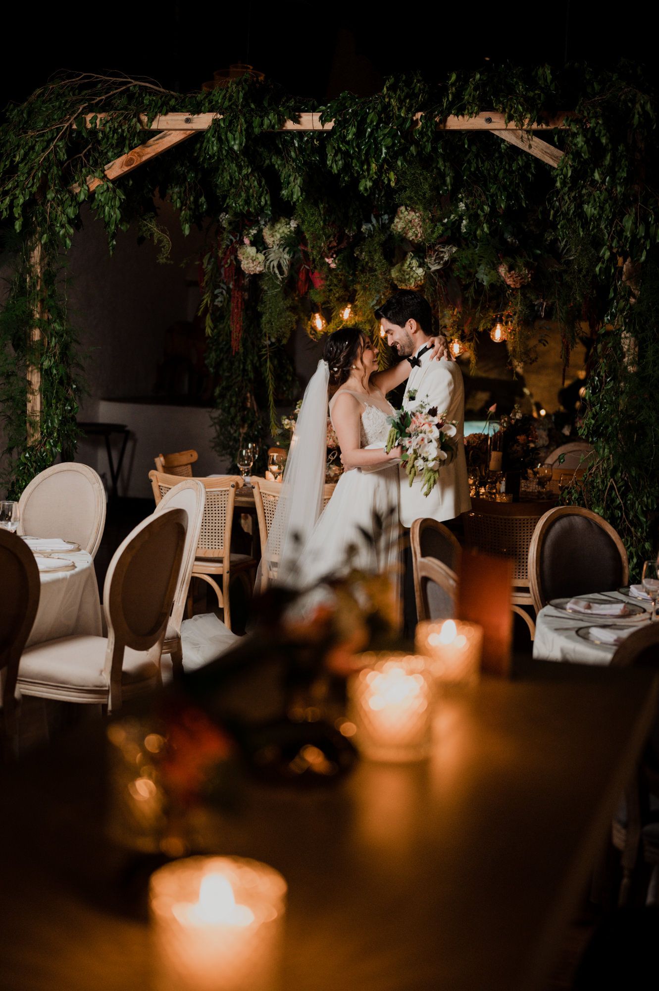 Wedding couple shares a moment under greenery and candlelight at their reception venue.