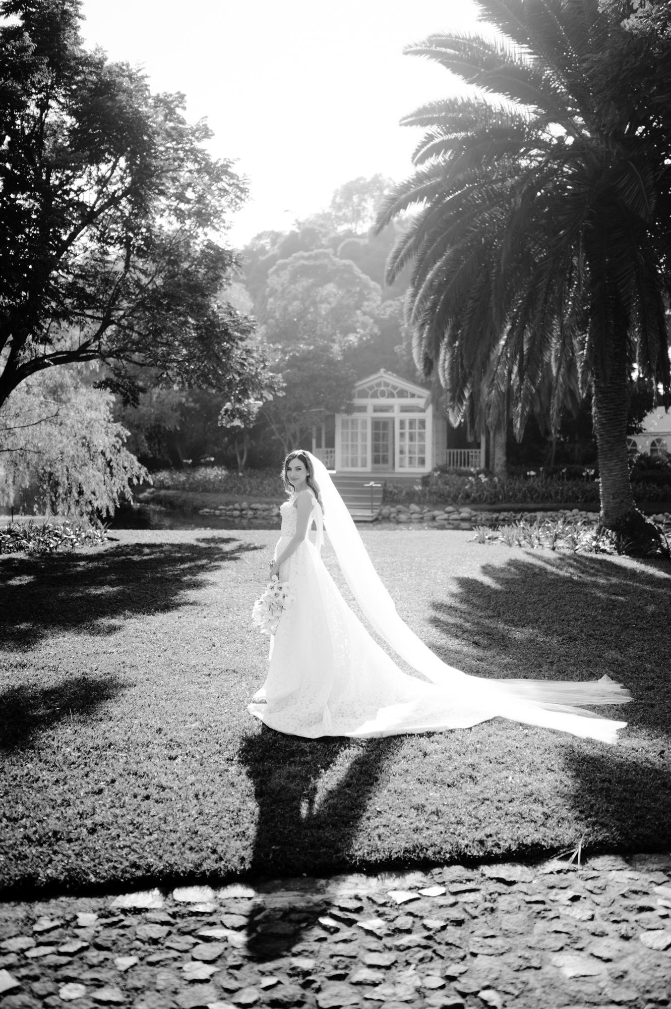 Dramatic black and white bridal portrait in garden setting with gazebo and palm trees.