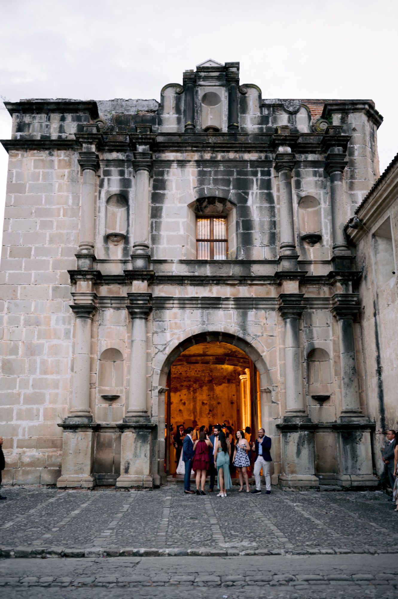 Historic stone church facade with ornate archway entrance and small group of visitors gathered at the door.