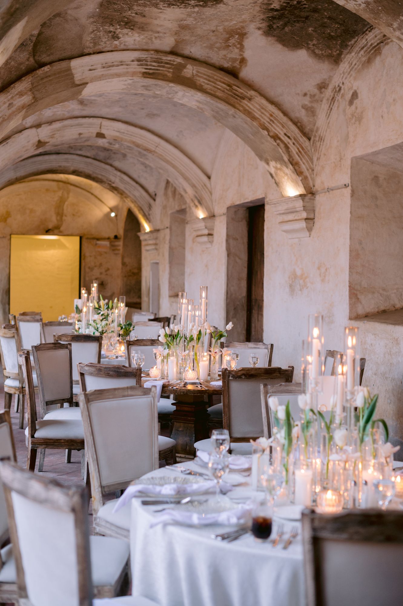 Intimate dining setup with candles and table settings in vaulted stone room.