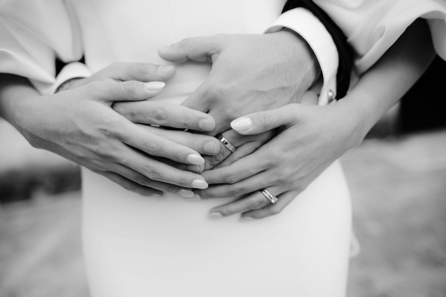 Close-up of hands with wedding rings intertwined in an intimate black and white photograph.