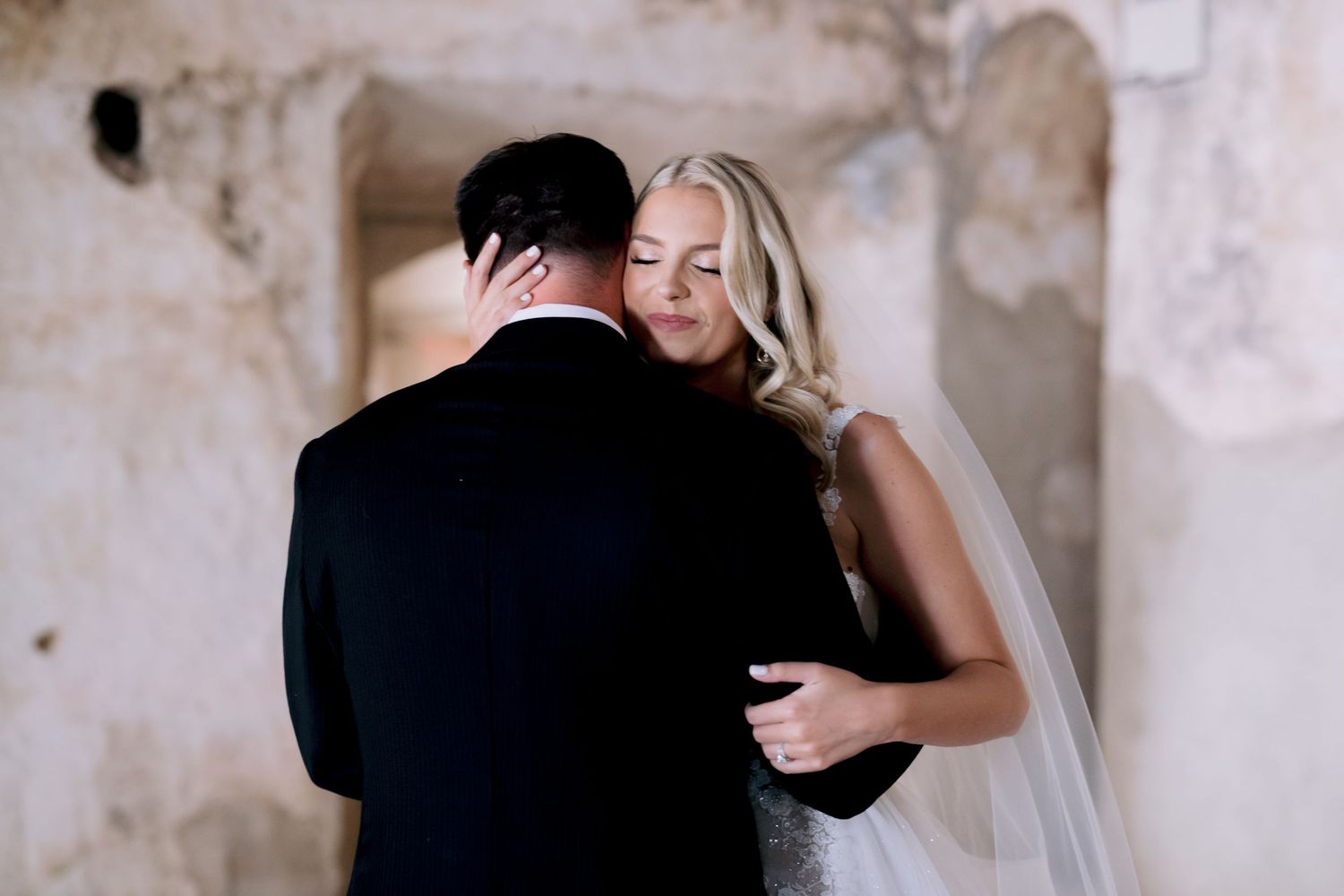 Tender wedding moment as couple embraces in a historic stone hallway.