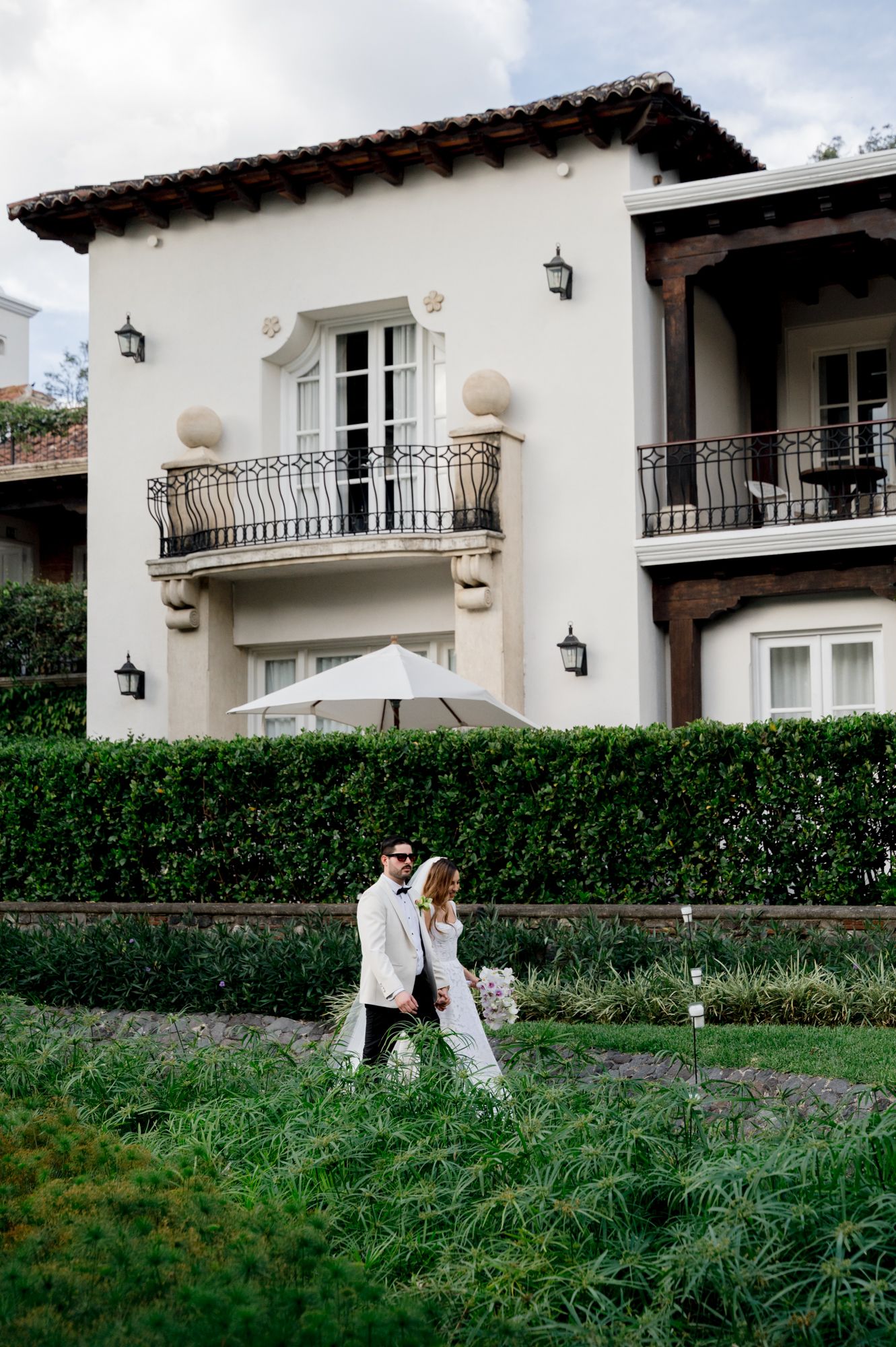 A couple walks together on landscaped grounds of an elegant white stucco building.