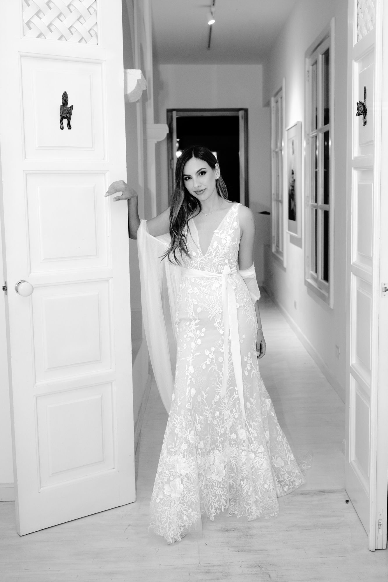 Black and white photo of a white lace dress flowing gracefully in a bright hallway with white walls.