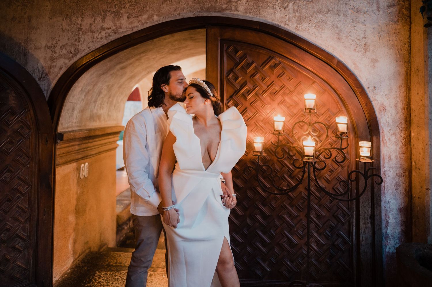 Couple sharing an intimate moment in a dimly lit stone archway with warm lighting.