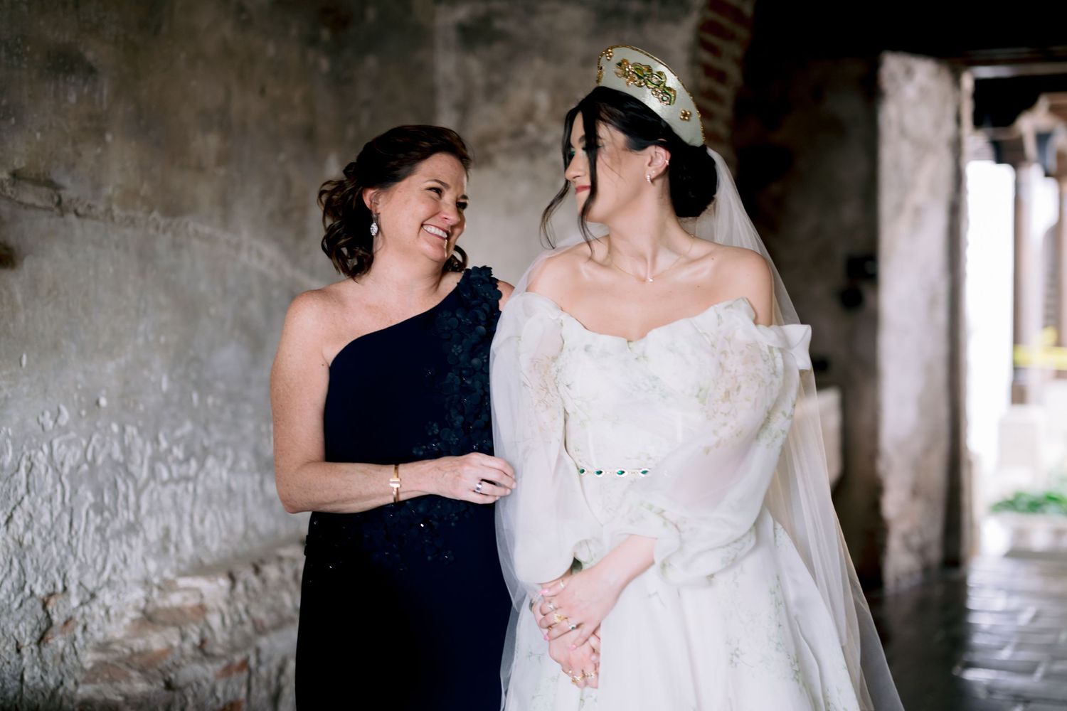 Two people share a joyful moment in formal attire against a textured wall background.