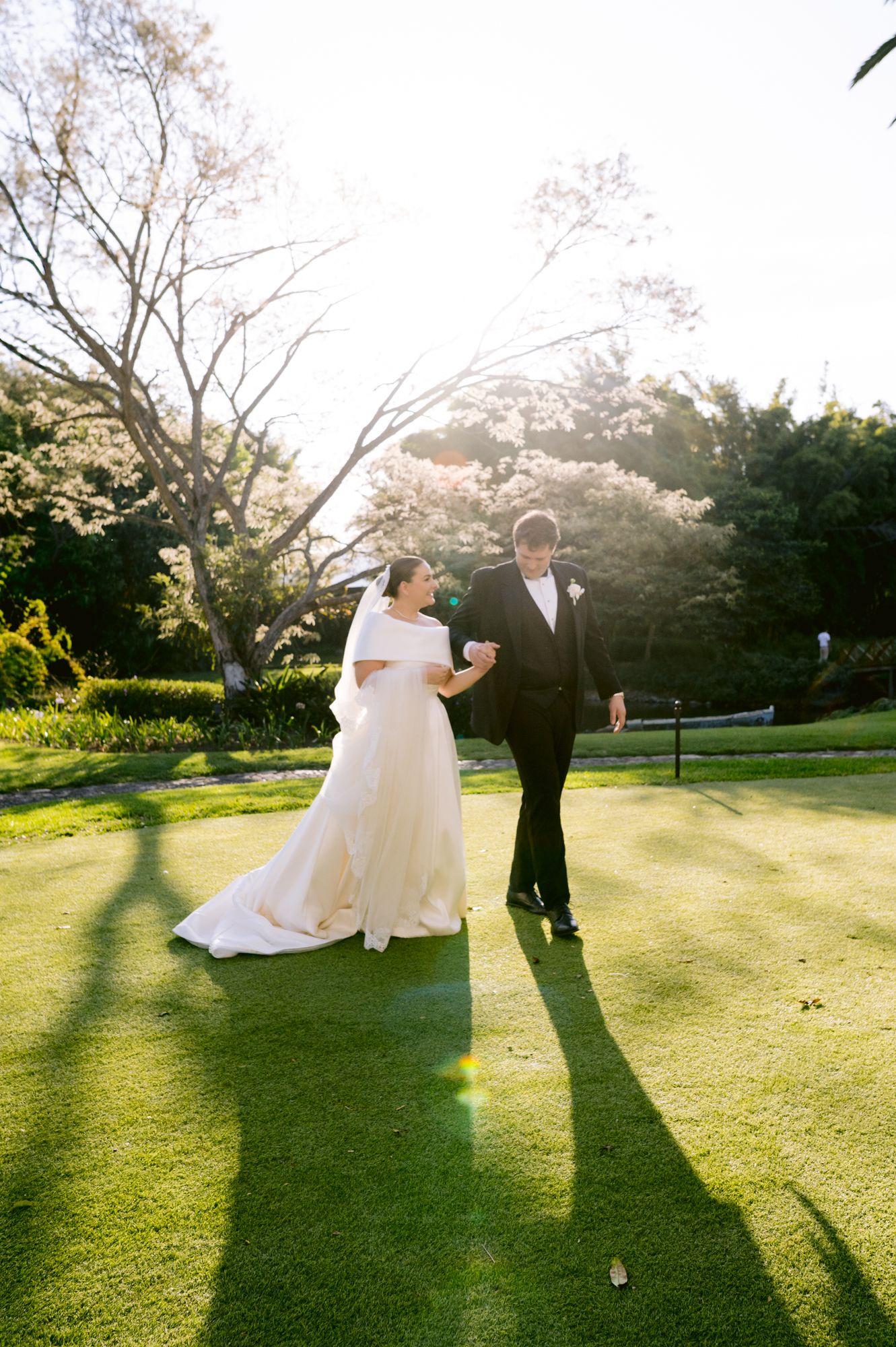 Sunset wedding photo of couple walking on manicured lawn with long shadows.