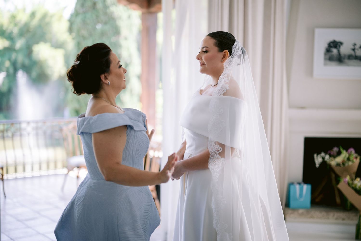 Bride in white dress sharing a moment with bridesmaid in light blue gown.
