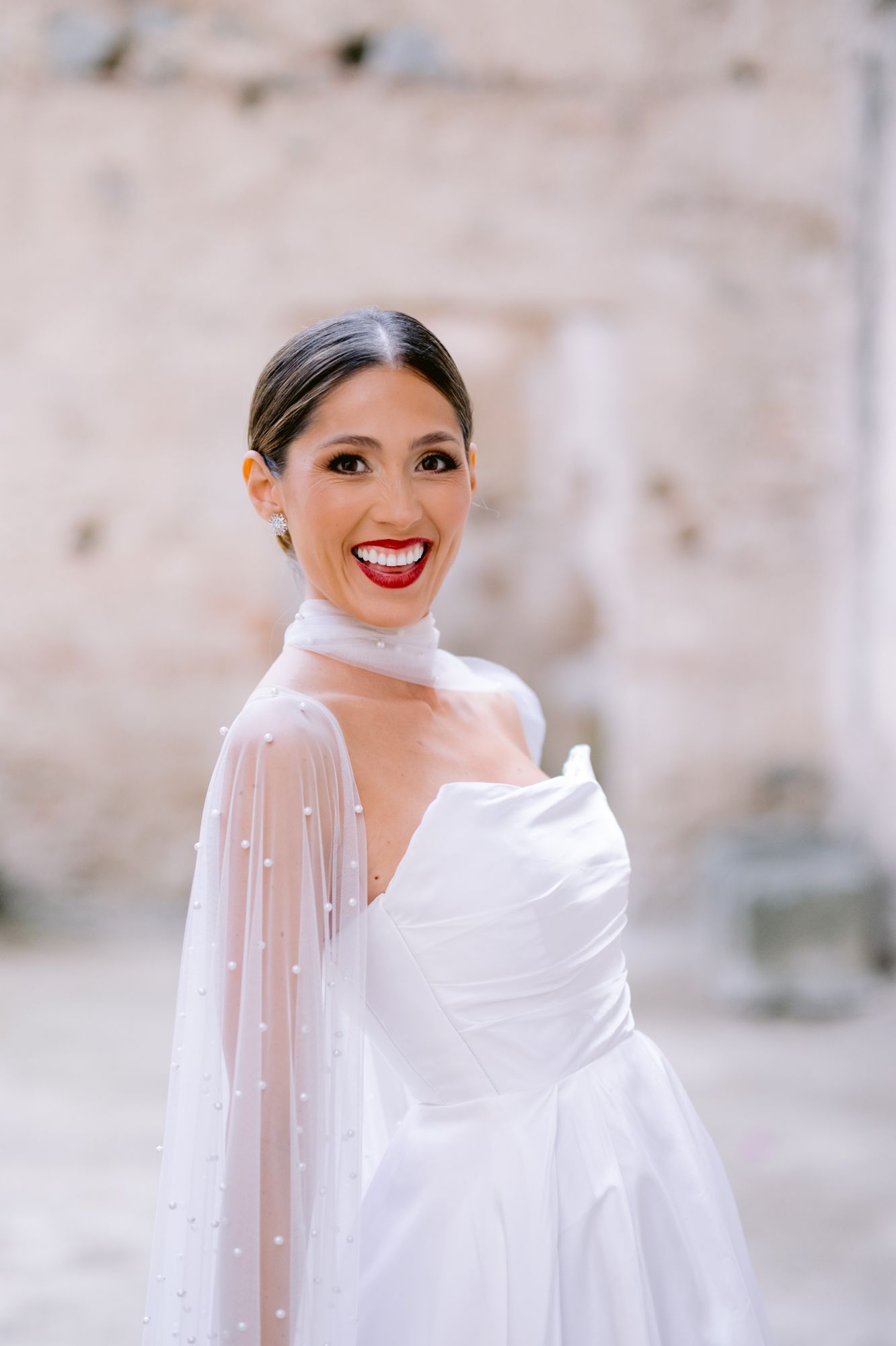 Close-up of bride wearing pearl-embellished sheer cape and classic white wedding gown.