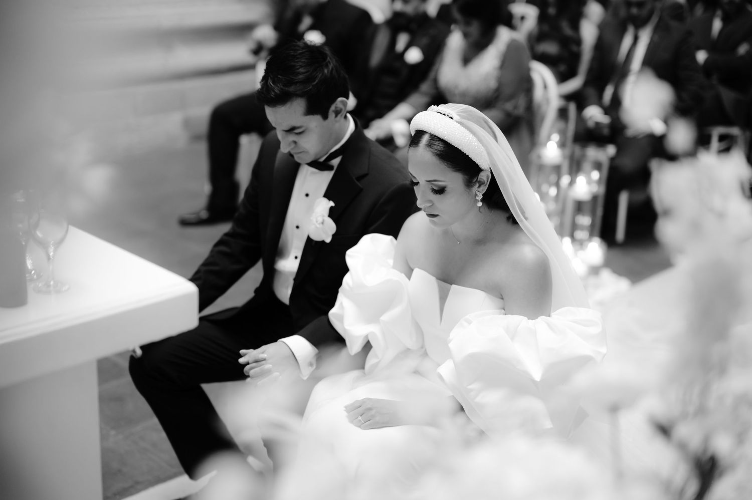 Intimate black and white wedding ceremony photo with couple seated amid soft candlelight.