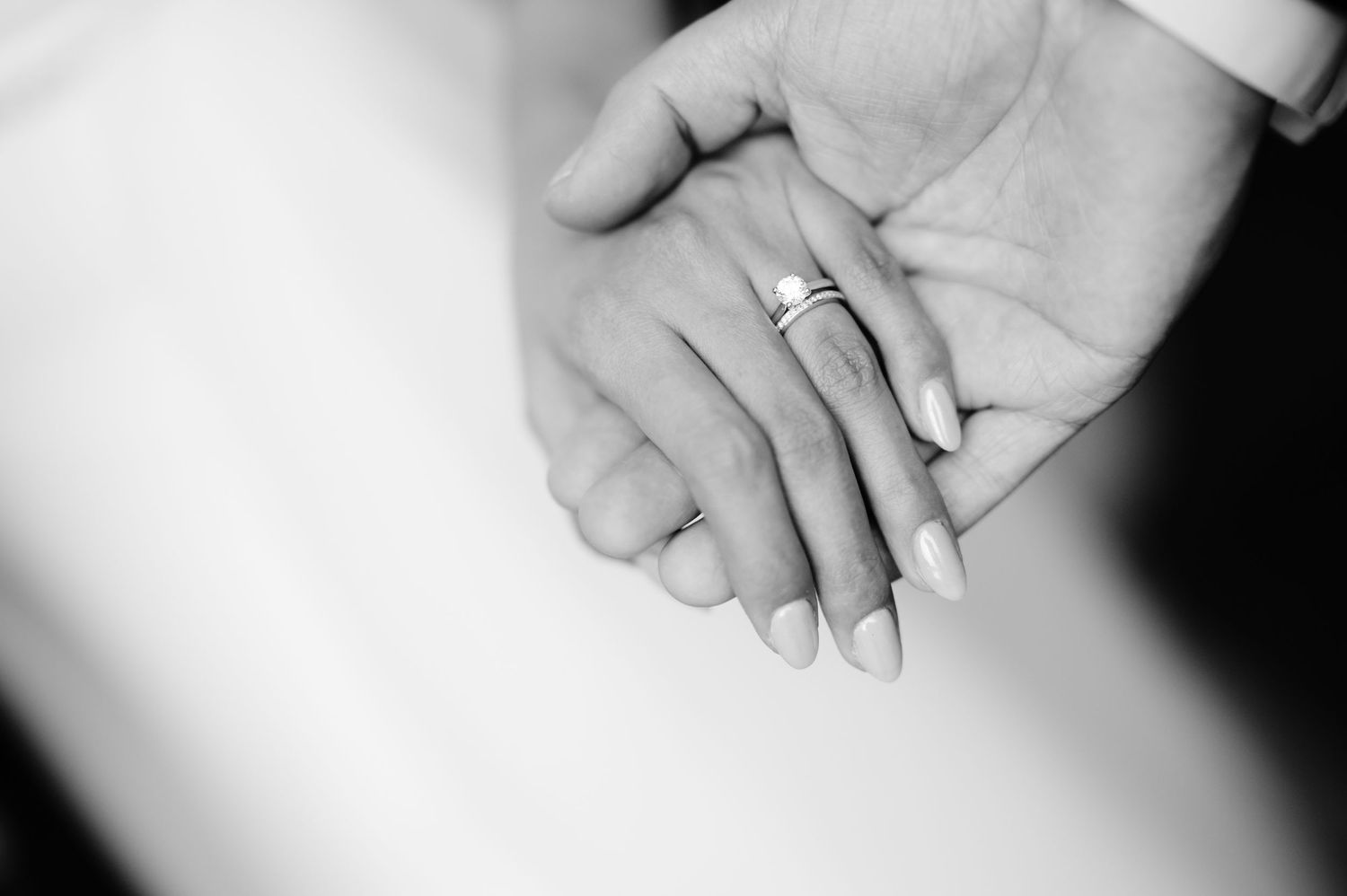 Close-up black and white shot of wedding rings and clasped hands.