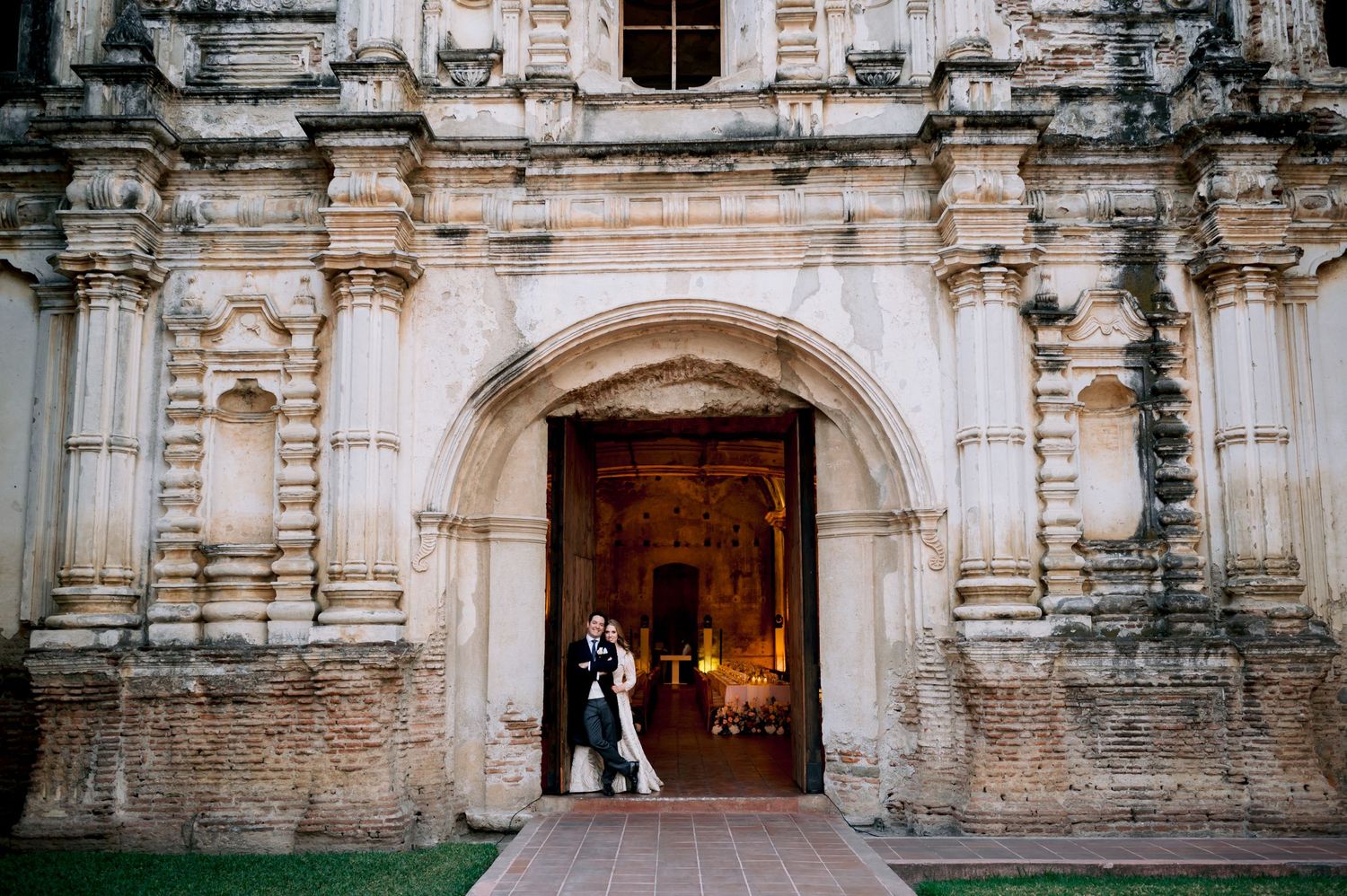 Newlyweds stand in a grand stone archway entrance of a historic building.