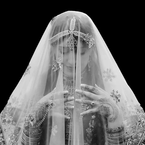 A figure draped in an ornate wedding veil with delicate lace details and embroidered patterns in black and white.
