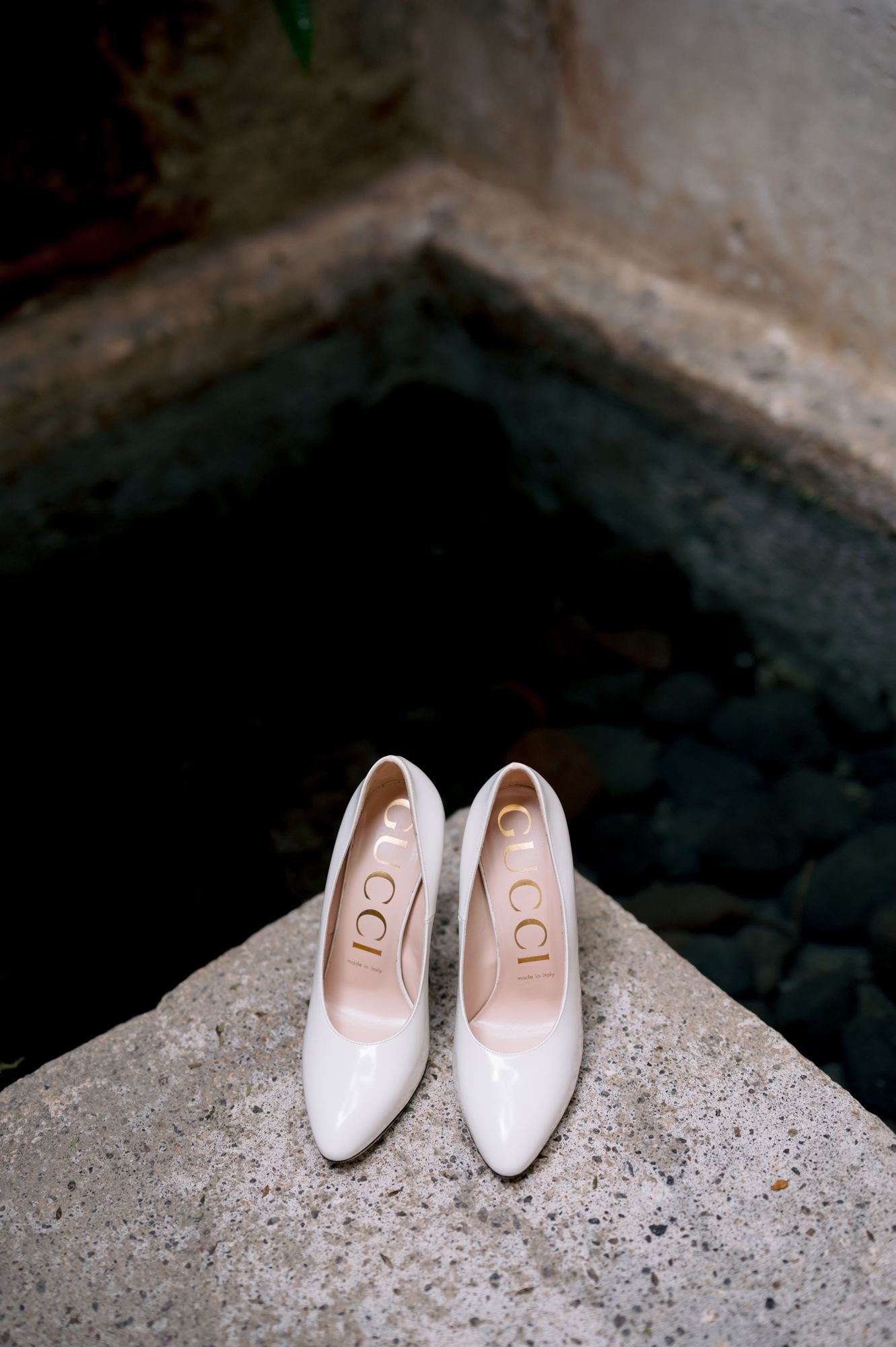 White bridal heels with GG logo placed on a stone ledge in dramatic lighting.