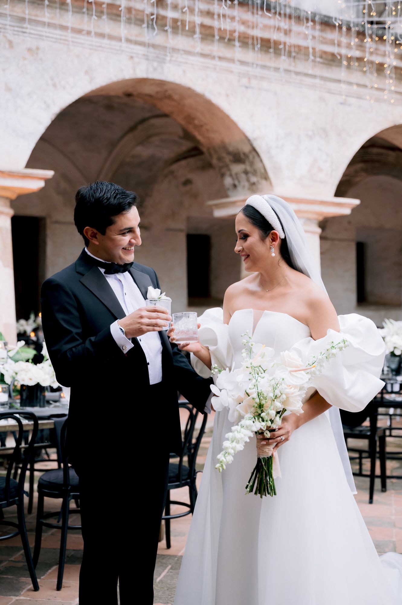 Wedding couple shares intimate moment while holding drinks under stone archway.