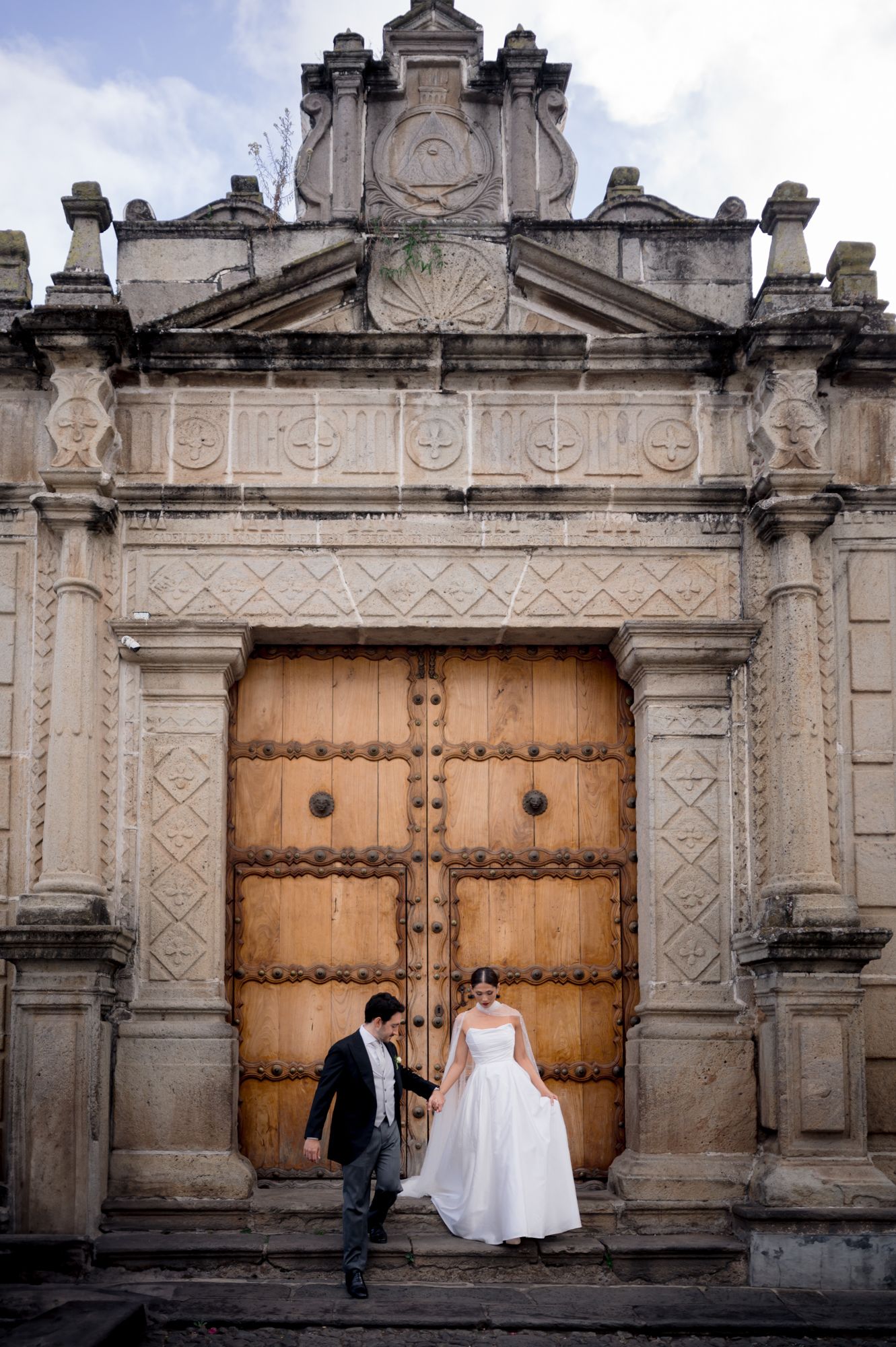 Wedding couple standing at grand colonial church entrance with carved stone details.