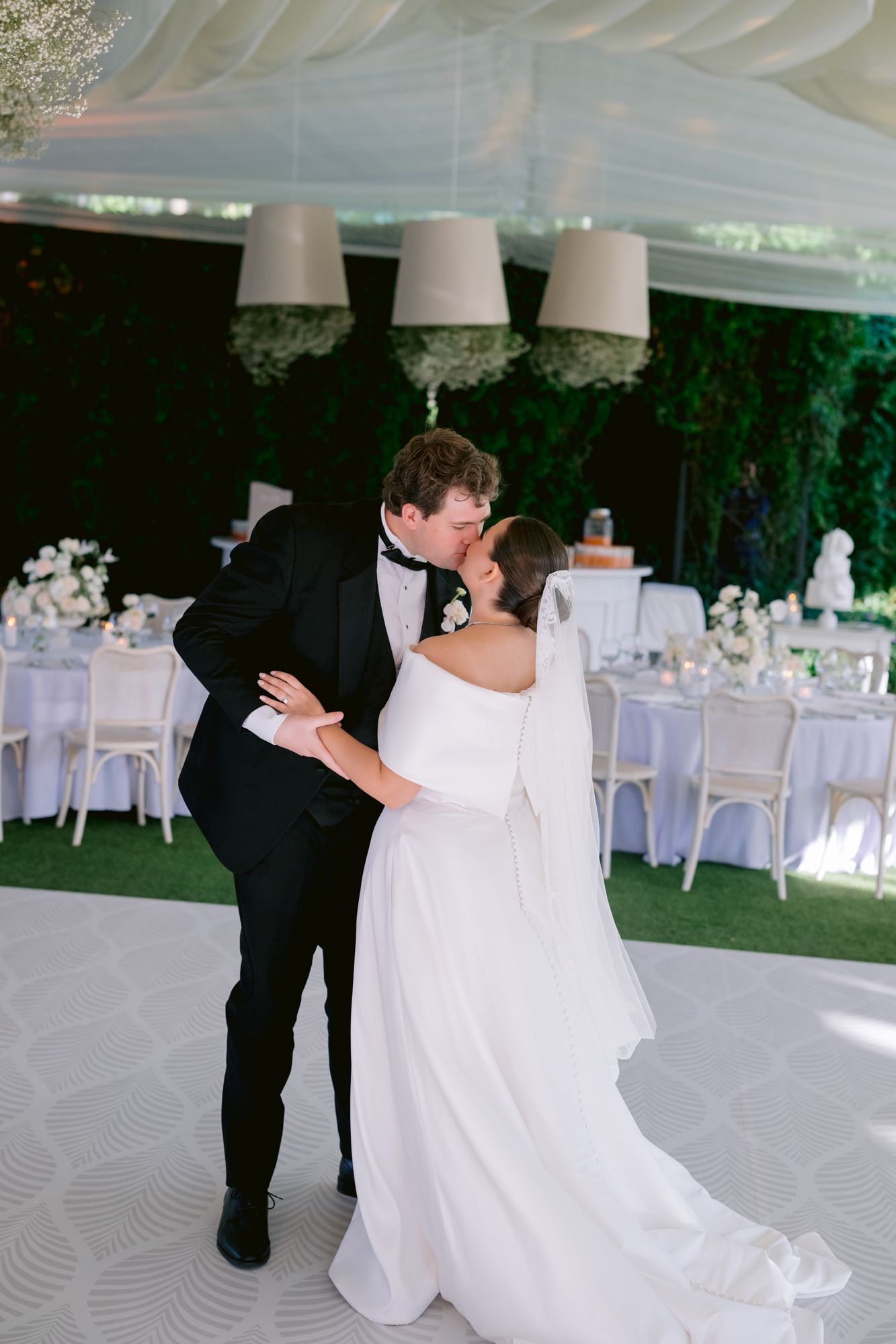 A newlywed couple shares their first dance under white pendant lights at an elegant outdoor wedding reception.