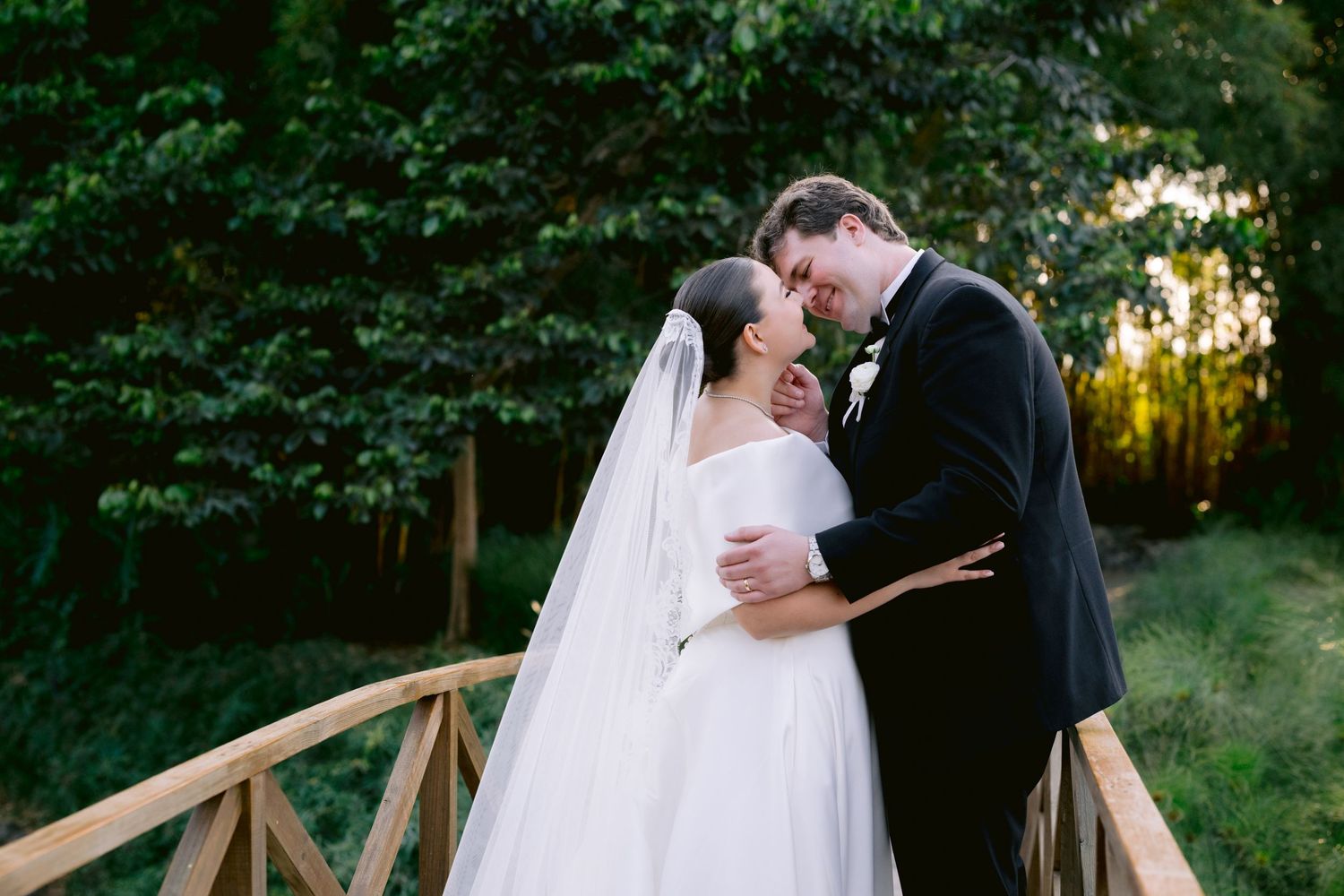 A tender moment between newlyweds on a wooden bridge surrounded by greenery.