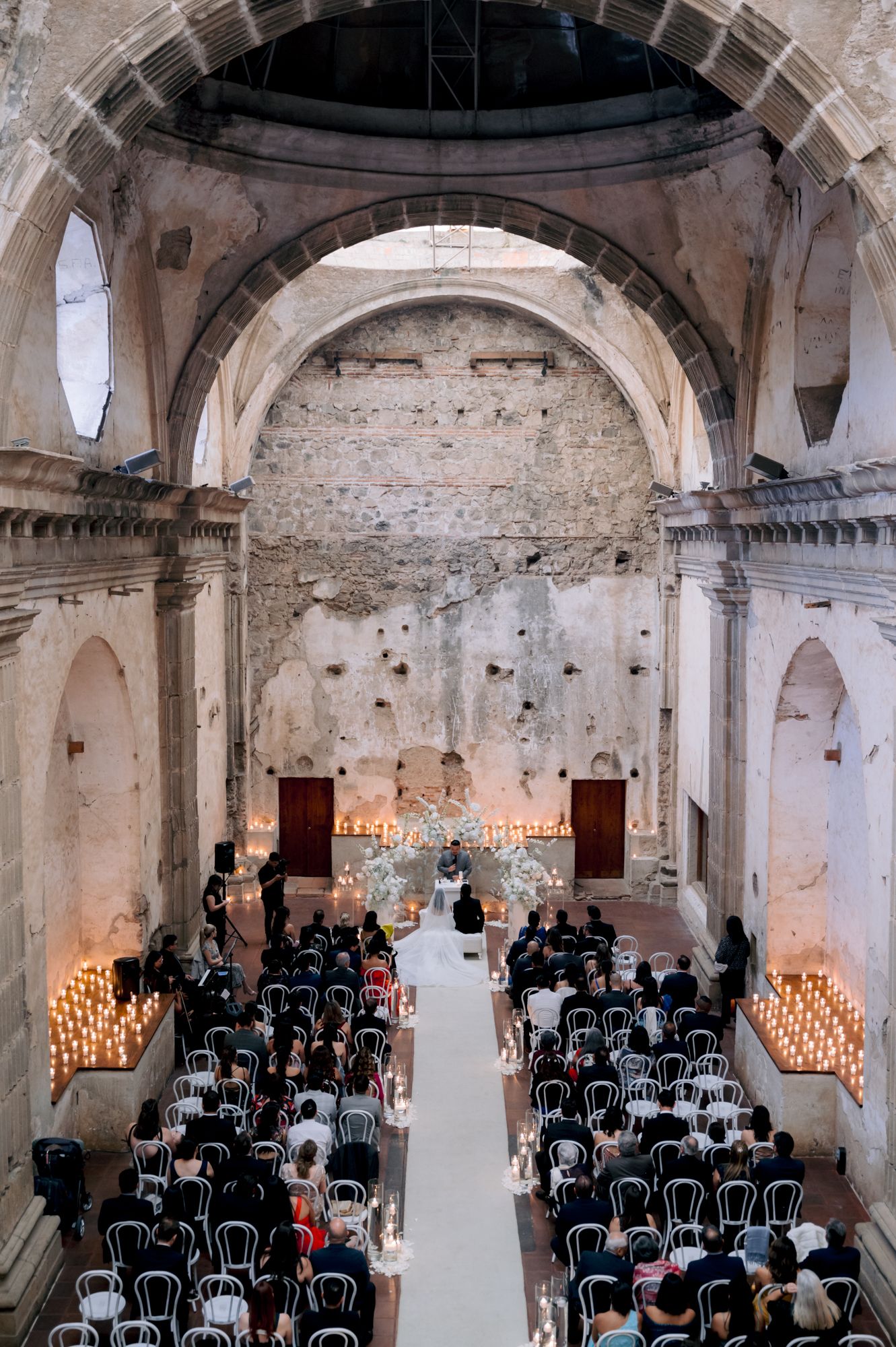 Wedding ceremony in rustic church with candlelit aisle and elegant white chairs.
