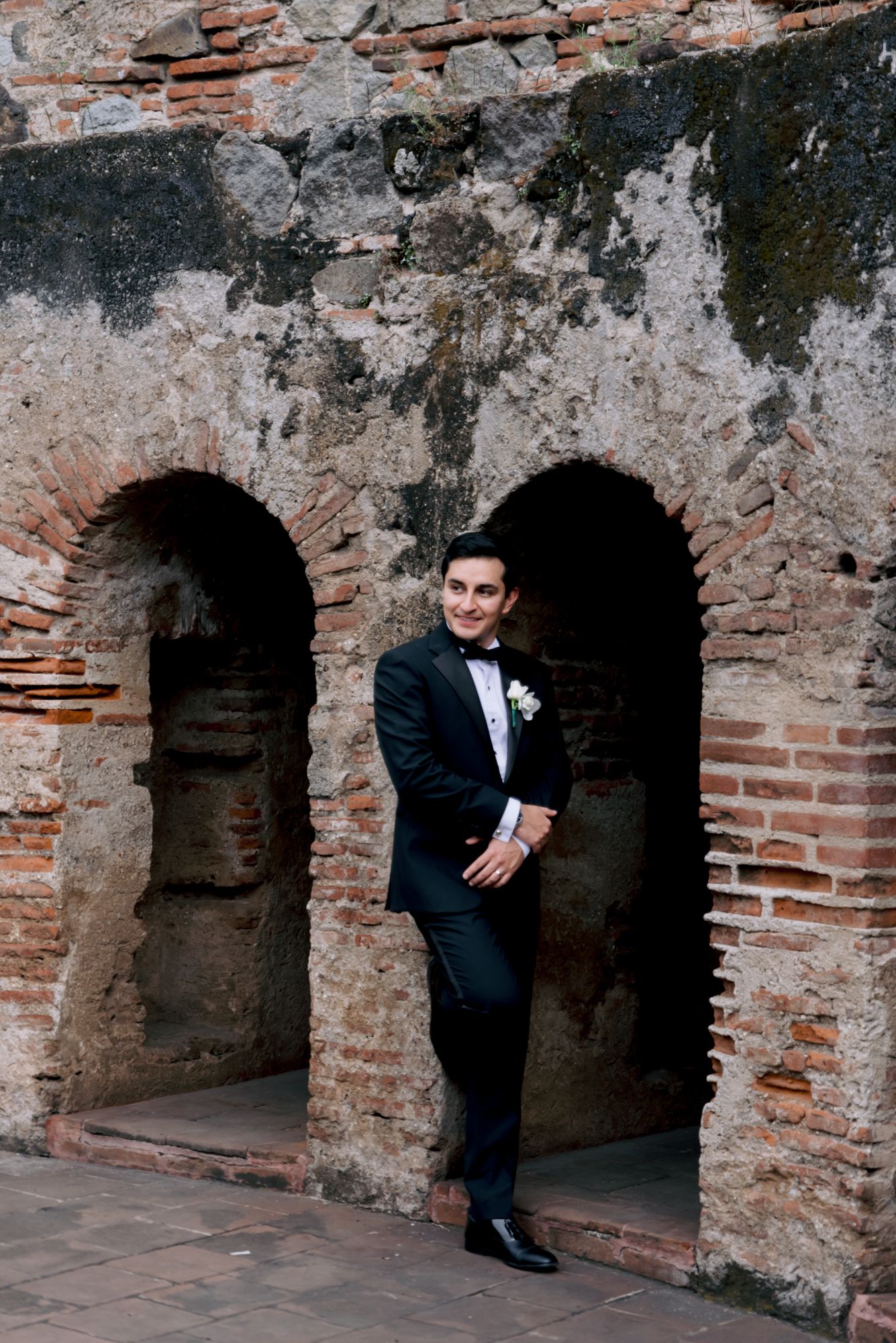 Classic groom portrait in dark suit framed by ancient brick archways.