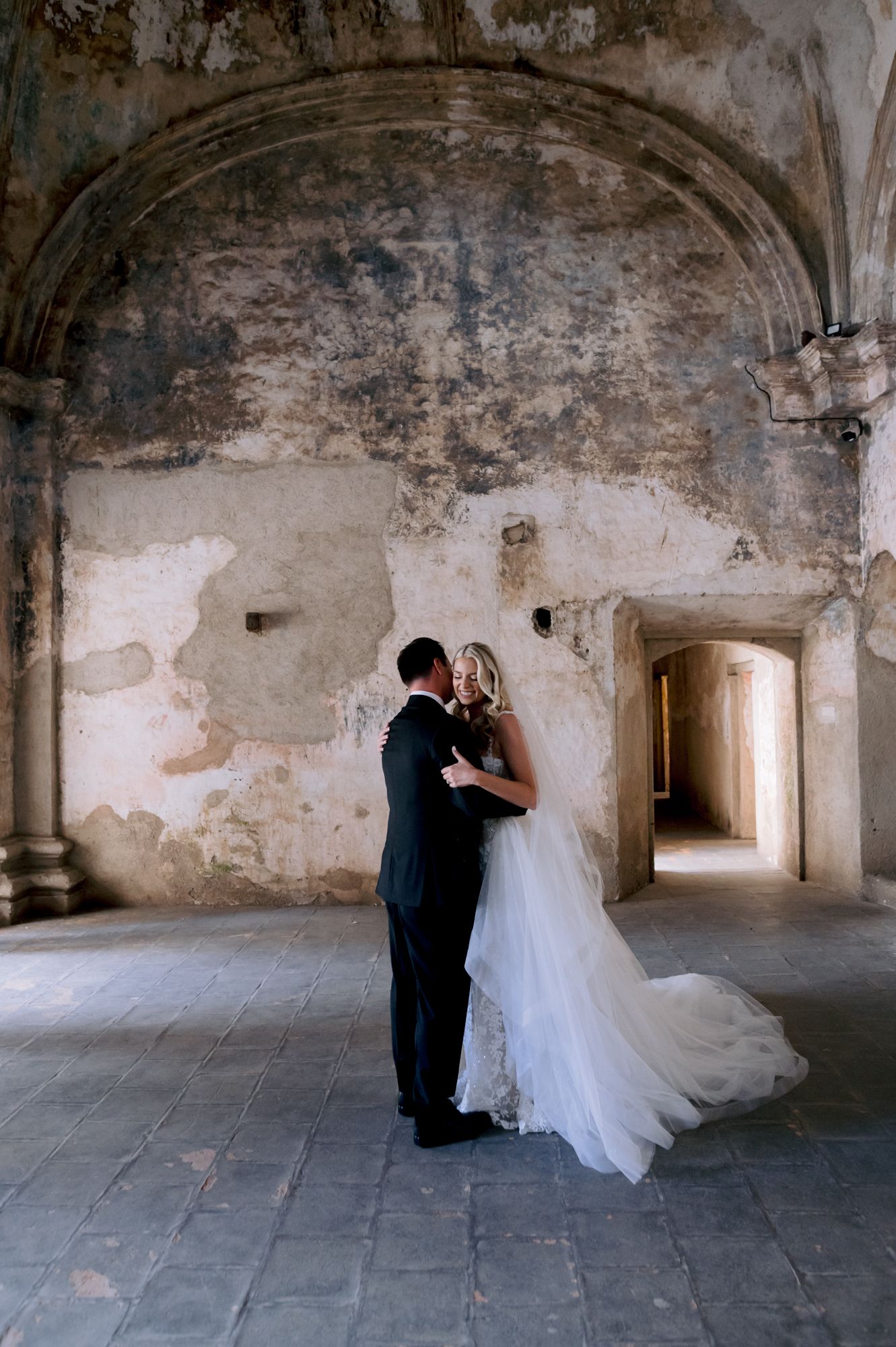 Newlyweds share intimate moment under weathered stone arch during wedding portraits.