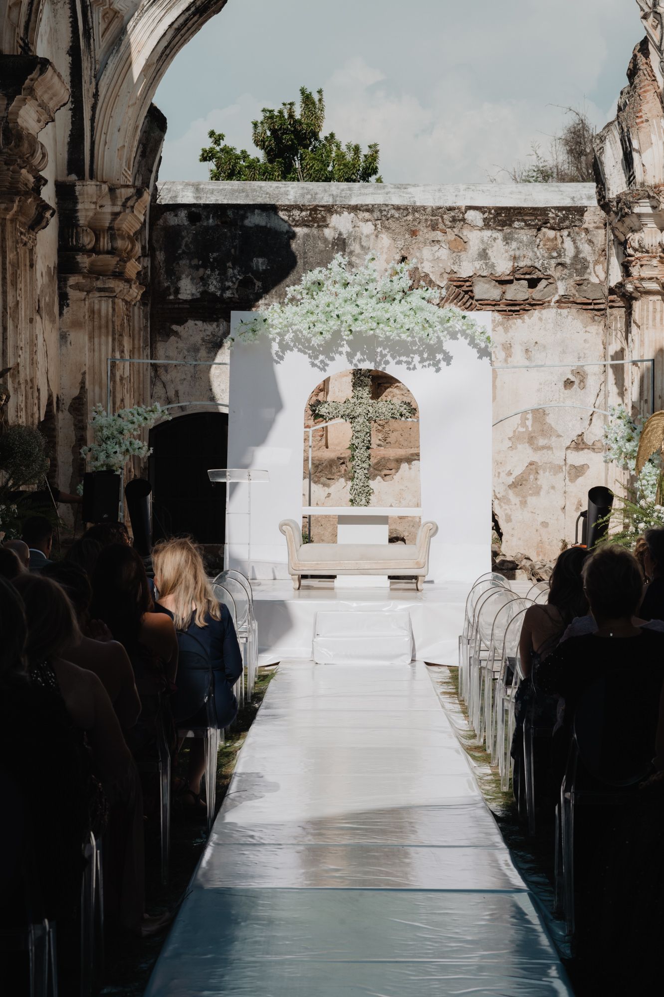A rustic wedding ceremony setup in an ancient stone building with white aisle runner and floral arch decorations.