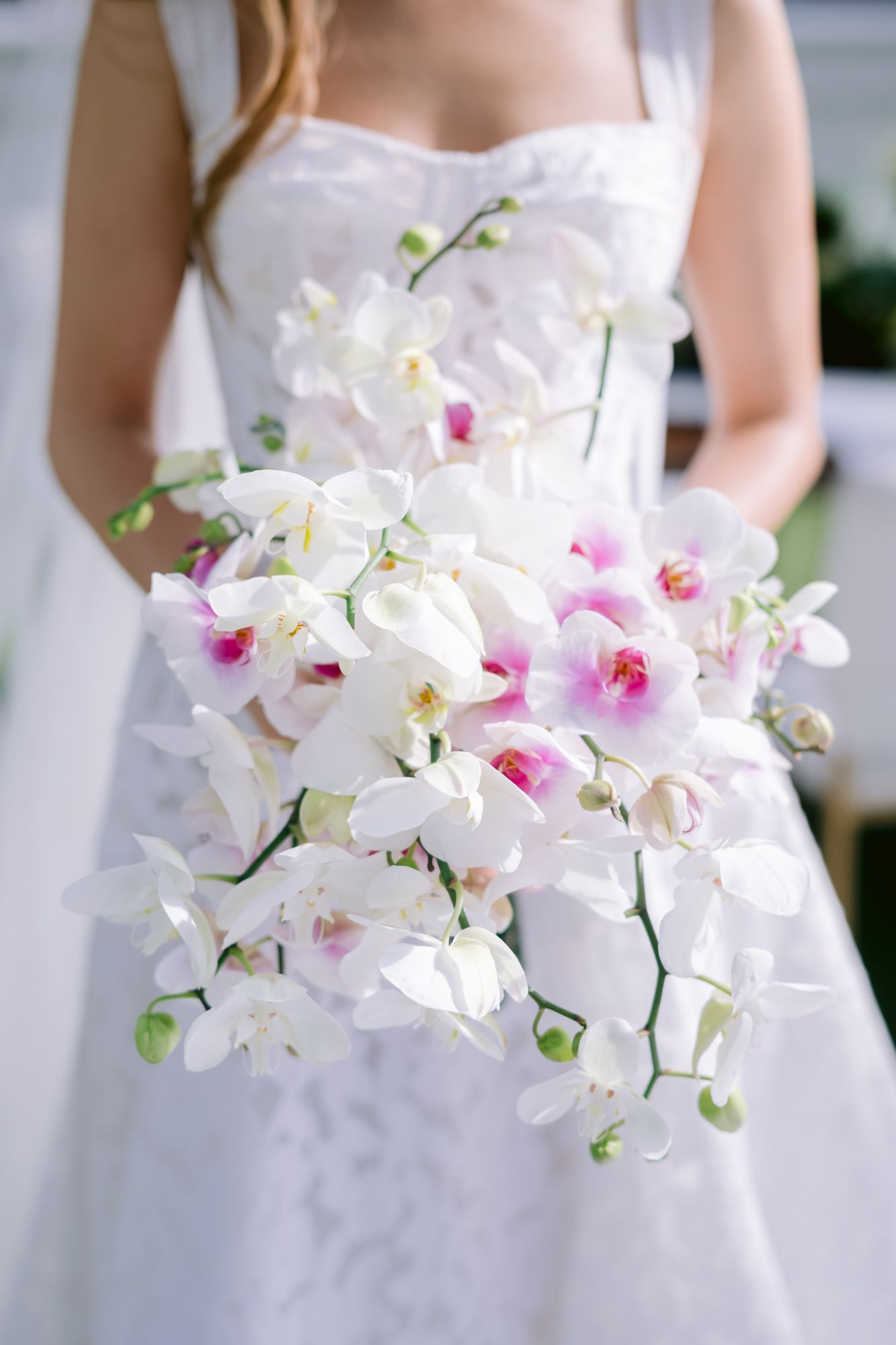 A stunning white and pink orchid wedding bouquet displayed against a white dress.